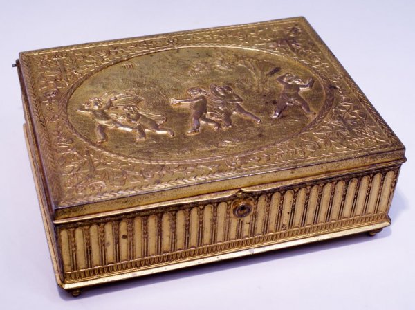 Fine Gilt Bronze Jewelry Box, Children Playing Hide-and: A fine c1900 gilt bronze jewelry box decorated with a classical scene of children playing Hide-and-Seek, 8" x 6" x 3"h, with an intricate reeded design around the sides. A heavy box with excellent hin