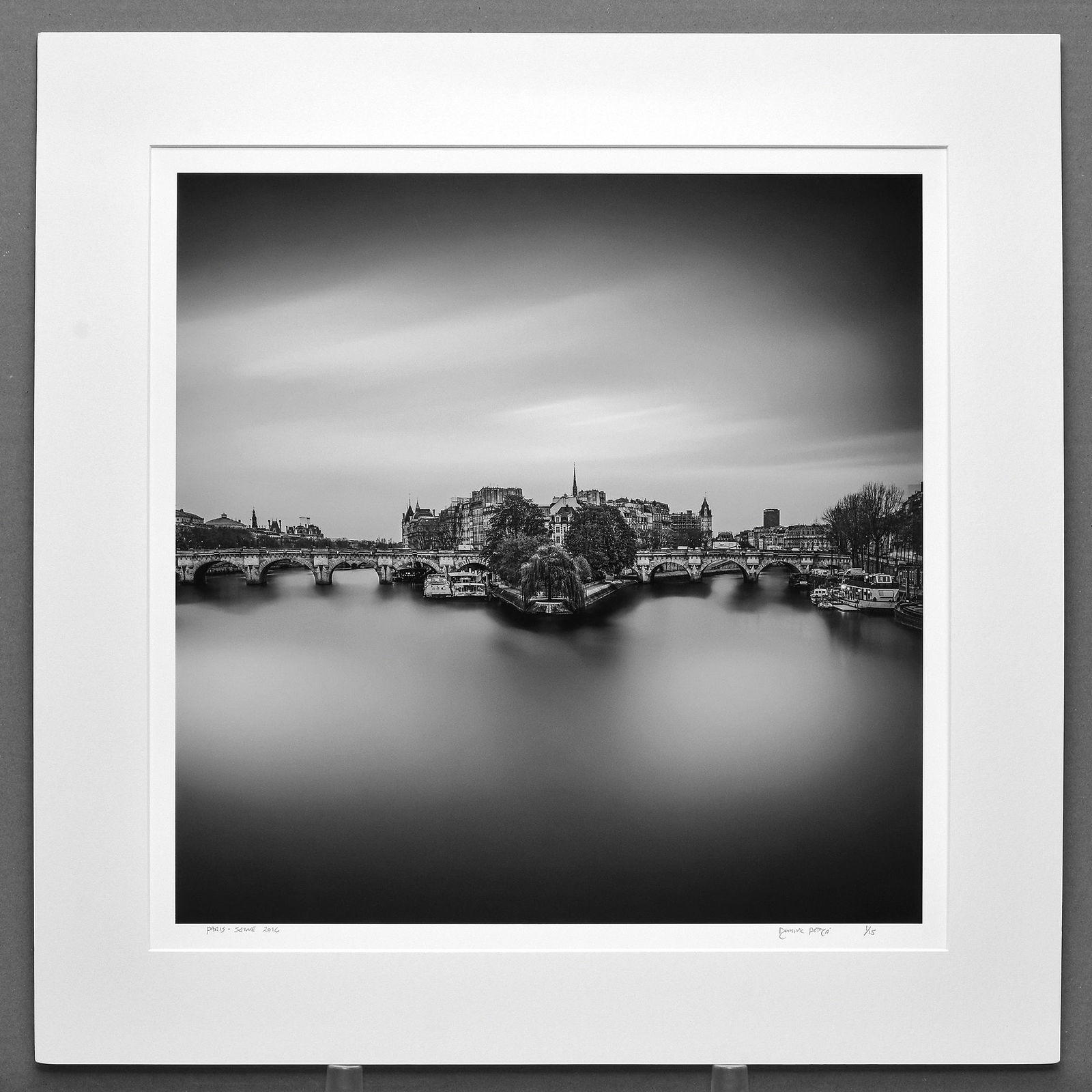 Dominic Petruzzi Signed 2016 Seine River - Paris France 16"x16" Photograph: This beautiful black-and-white image by Petruzzi captures the timeless atmosphere of Paris along the Seine, created using a slow shutter speed that transforms the flowing water into a luminous, dreaml