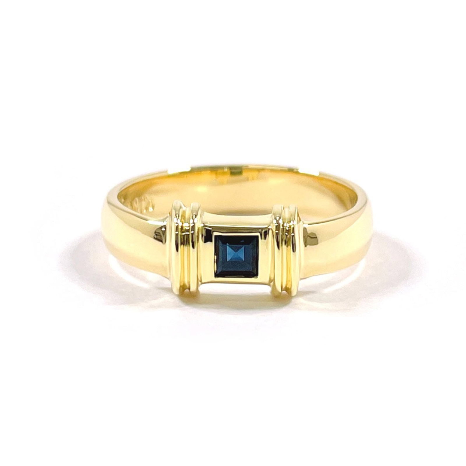 (18K) Tiffany Band Ring Yellow Gold: (18K) Tiffany Band Ring Yellow Gold A stunning 18K yellow gold Tiffany band ring, adorned with a vibrant blue sapphire stone, adds a touch of elegance to any outfit. With its classic design and high-q