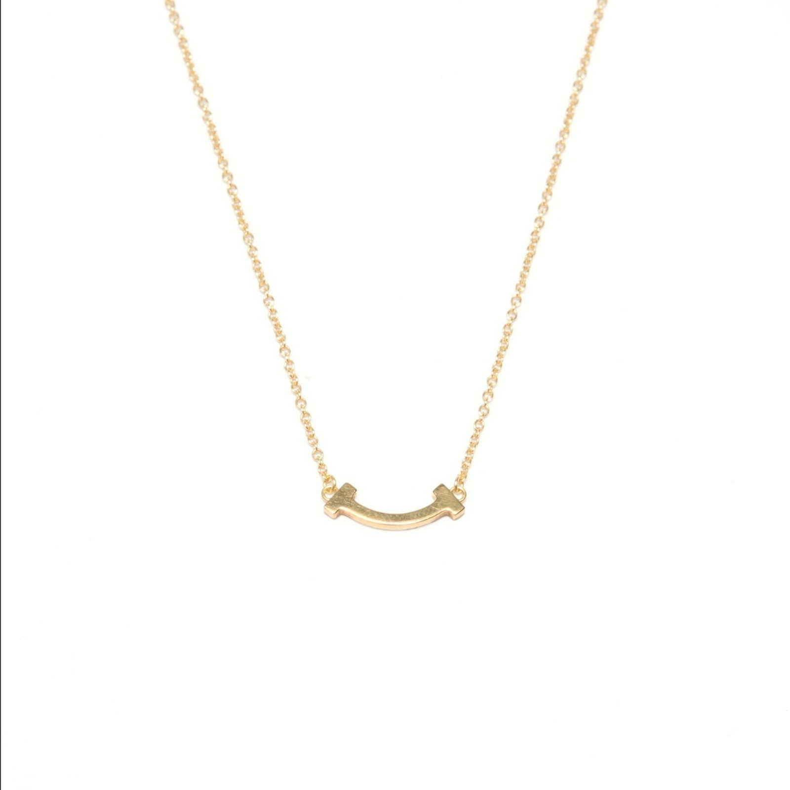 WS24850 - Tiffany & Co. Au750 T Smile Necklace - Gold: WS24850 - Tiffany & Co. Au750 T Smile Necklace - Gold A stunning Tiffany & Co. Au750 T Smile Necklace in gold, boasting a sleek 12mm x 15mm pendant that adds a touch of sophistication to any outfit. W