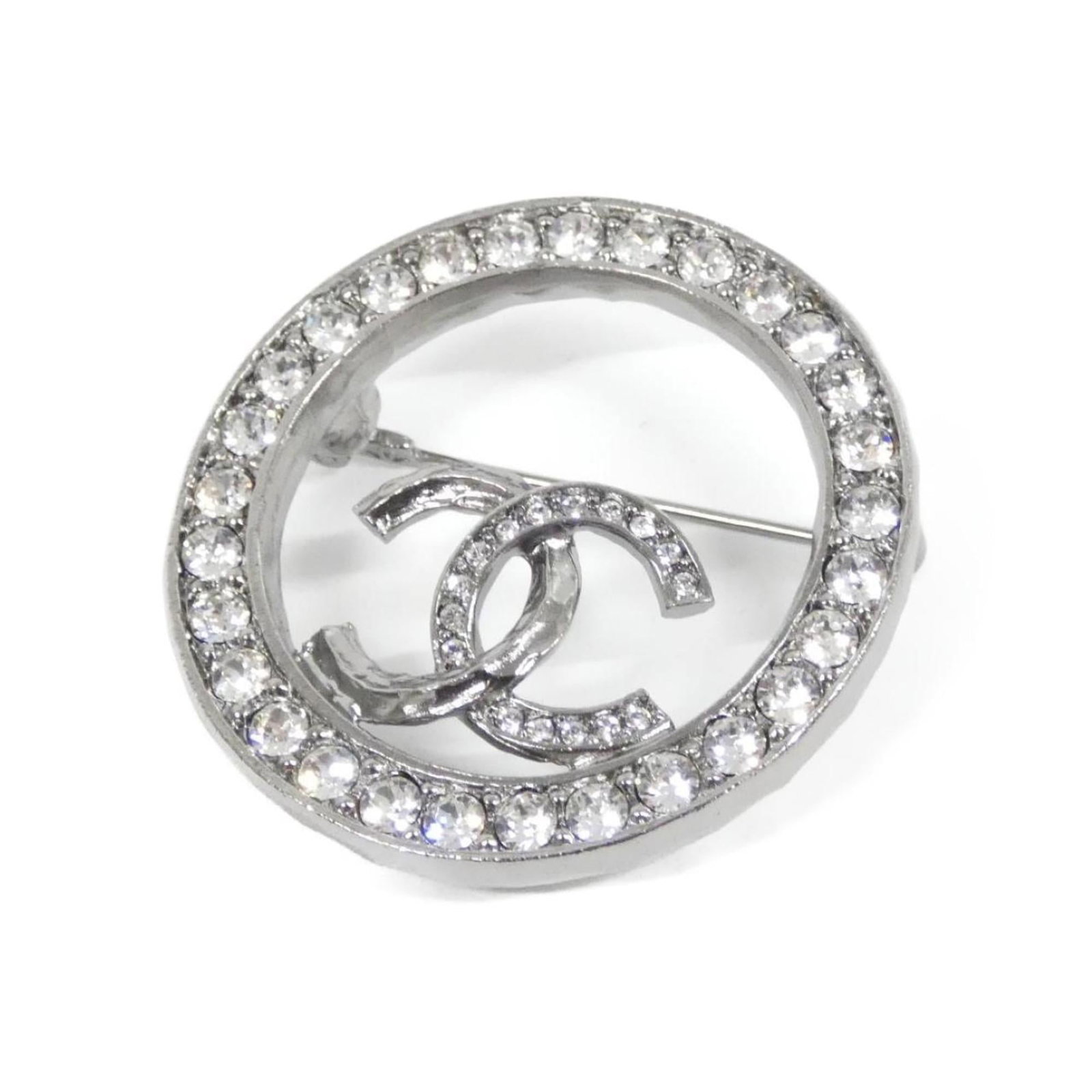 Brooch Chanel: Brooch Chanel A stunning silver Chanel brooch, adorned with crystal accents, adds a touch of timeless elegance to any outfit. Its sleek design and subtle sparkle make it a versatile accessory for form