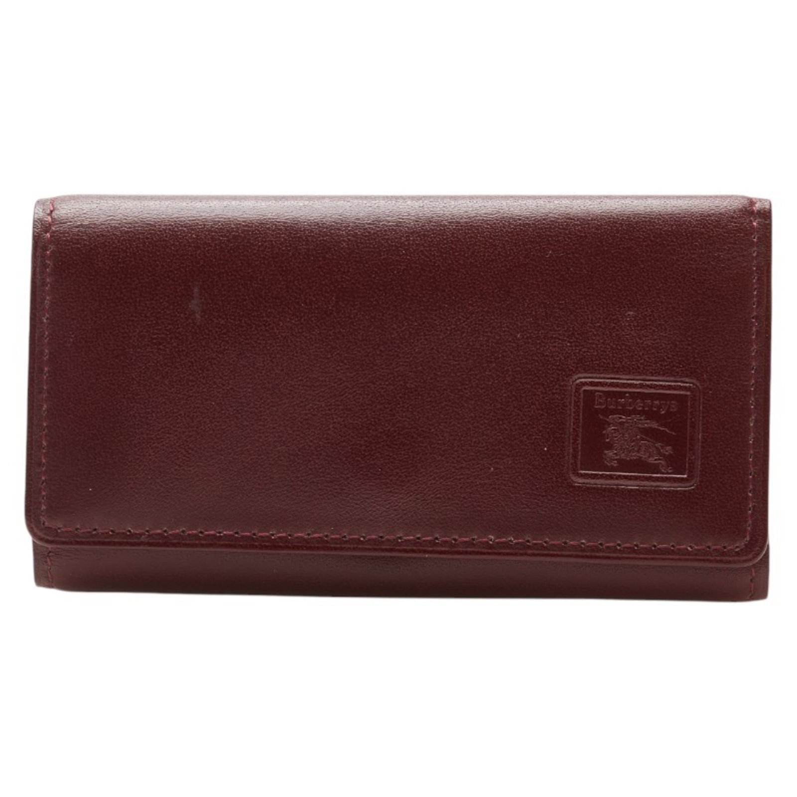 Burberry Keycase Leather: Burberry Keycase Leather Burberry Keycase Leather is a used women's leather keycase in Bordeaux color. It features scratches and dirt, with traces of usage, yet remains generally in good condition.