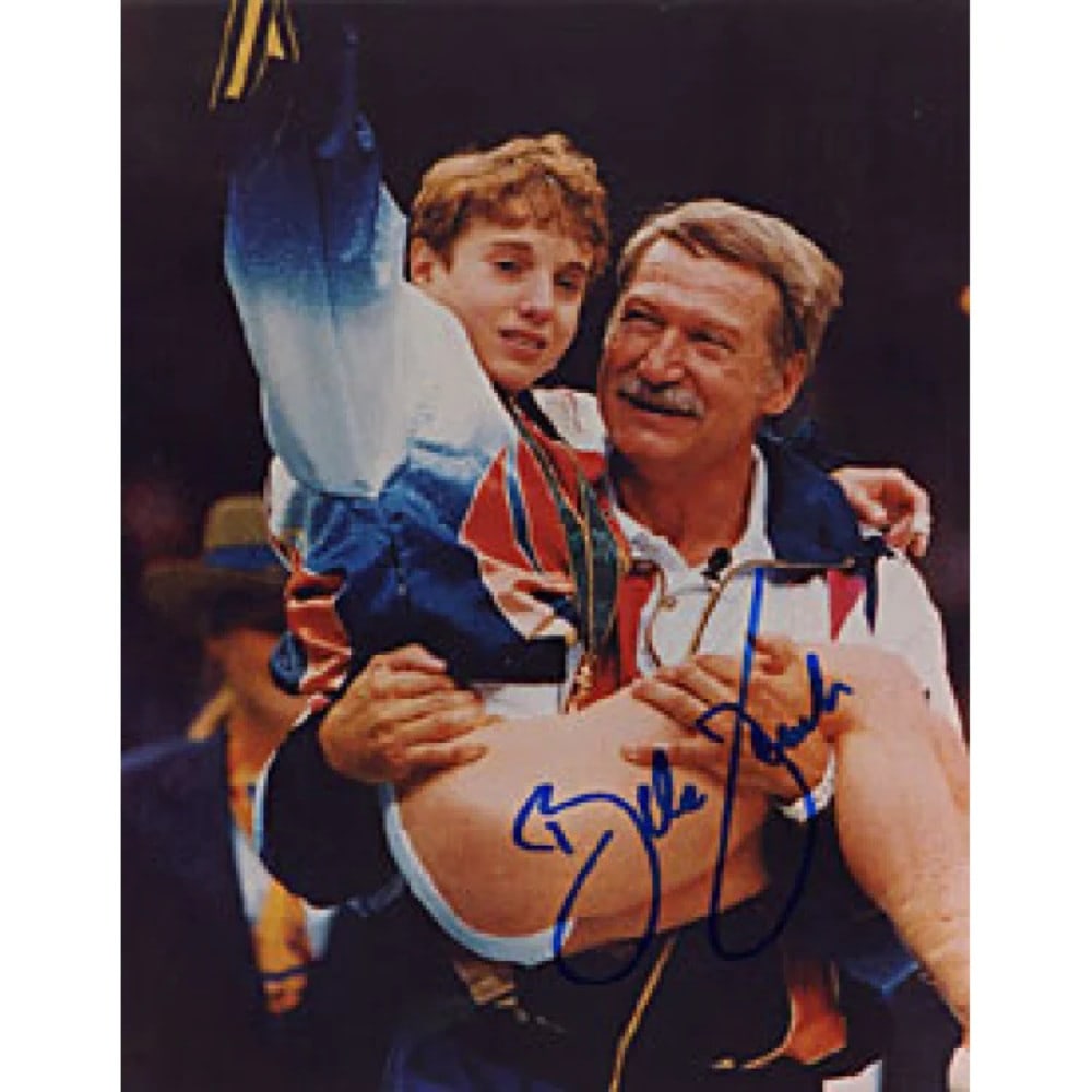 STRUG KERRI AUTIGNED 810 PHOTO: STRUG KERRI AUTIGNED 810 PHOTO Color 8x10 photo of Kerri Strug being held by her coach Bela Karolyi after winning at the 1996 Summer Olympics. The image captures a momentous victory, with Strug's sign