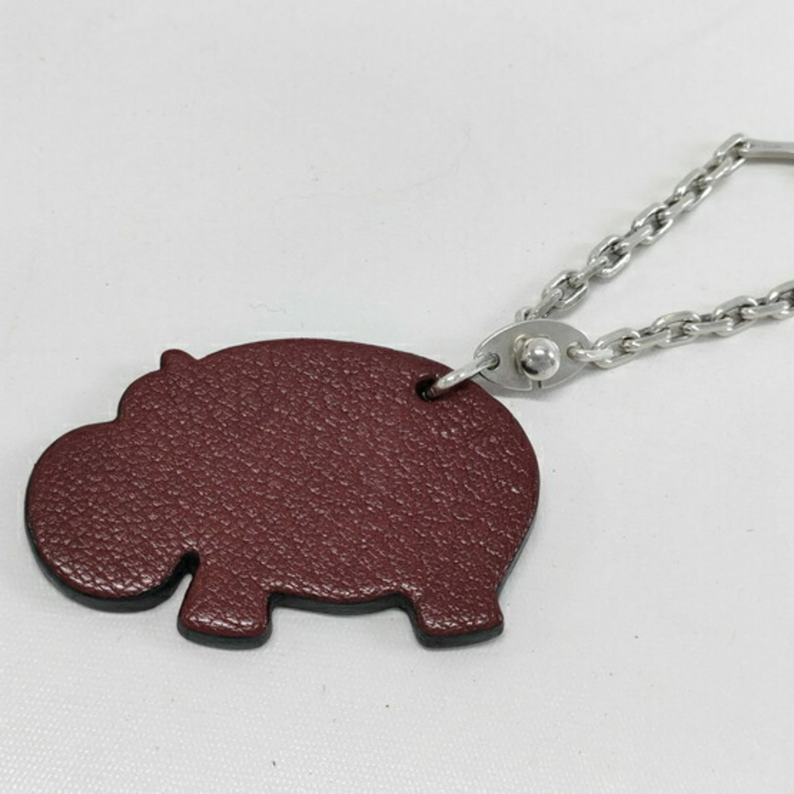 Hermes handbag charm leather: Hermes handbag charm leather Brown and red leather handbag charm with a rich, worn appearance. The charm measures 35mm x 55mm and features some scratches and dirt, giving it a well-used look. Overall,
