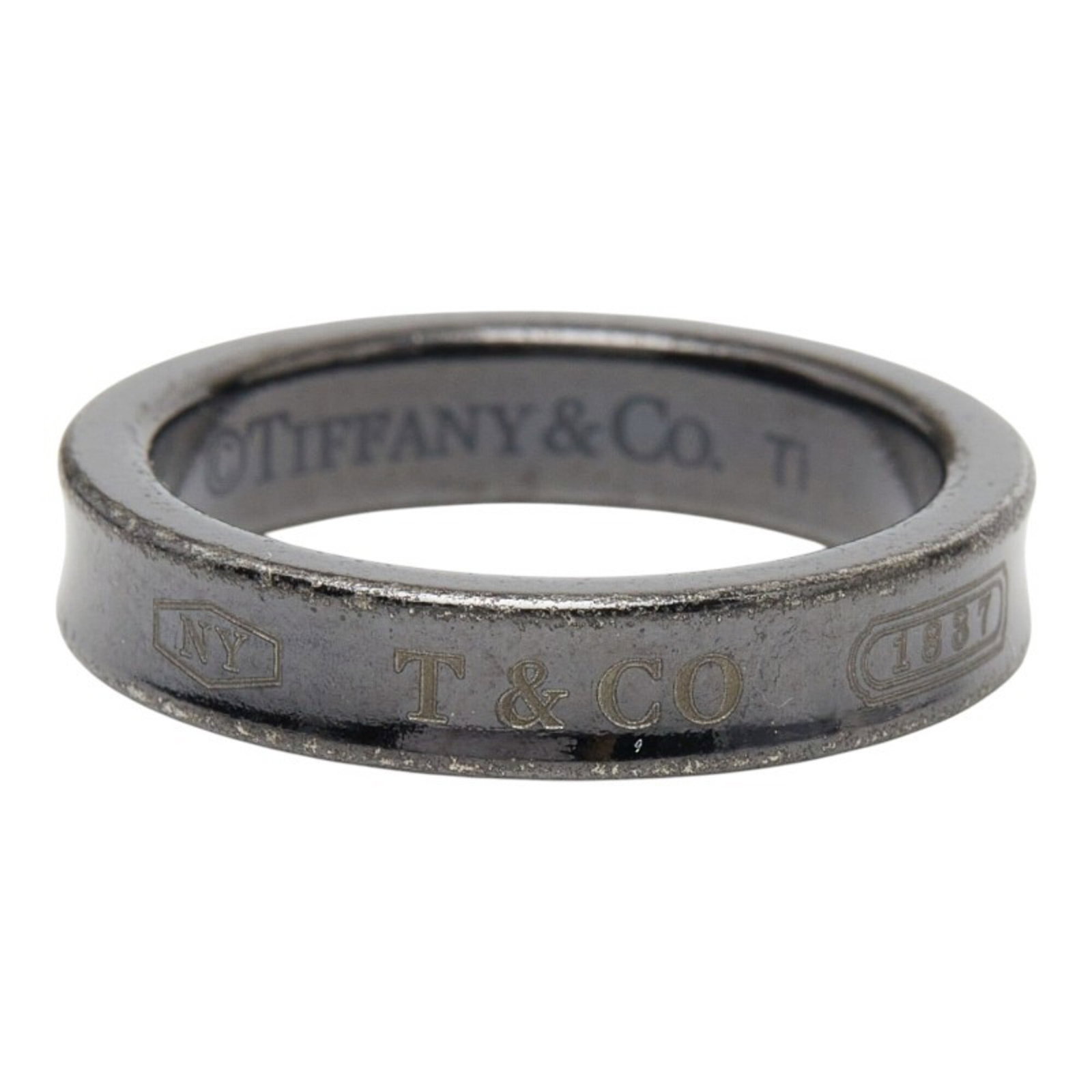 Tiffany Band Ring Titanium: Tiffany Band Ring Titanium Titanium band ring with a sleek black finish, bearing the Tiffany brand. This used item shows signs of wear and has minor scratches, but remains in good condition overall. A