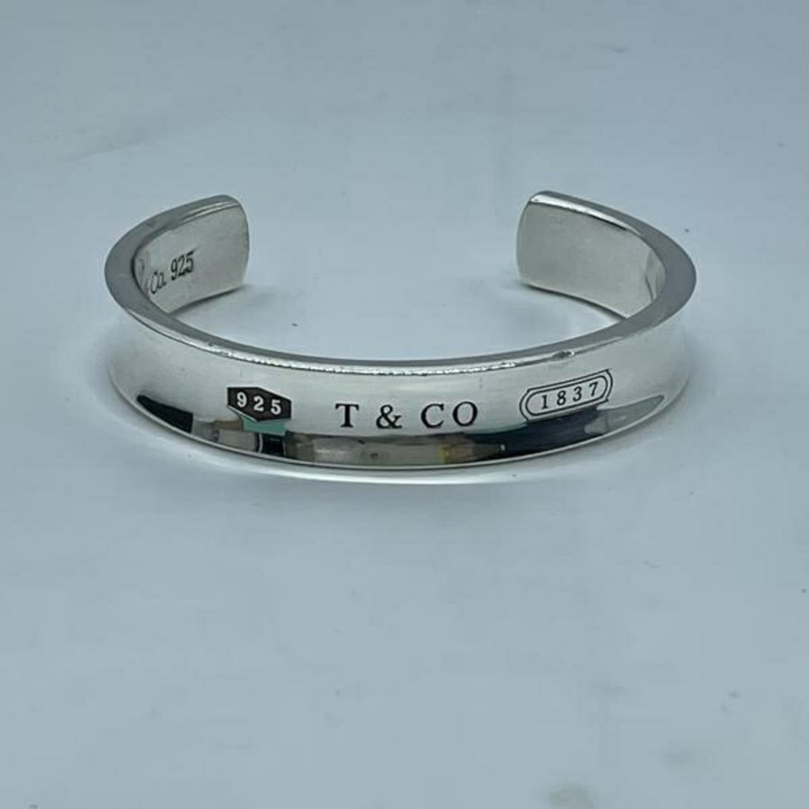 Tiffany Bangle: Tiffany Bangle Tiffany's iconic bangle boasts a sleek silver finish and durable design, measuring 15.5cm in length. With traces of usage visible, this pre-owned bangle still retains its original