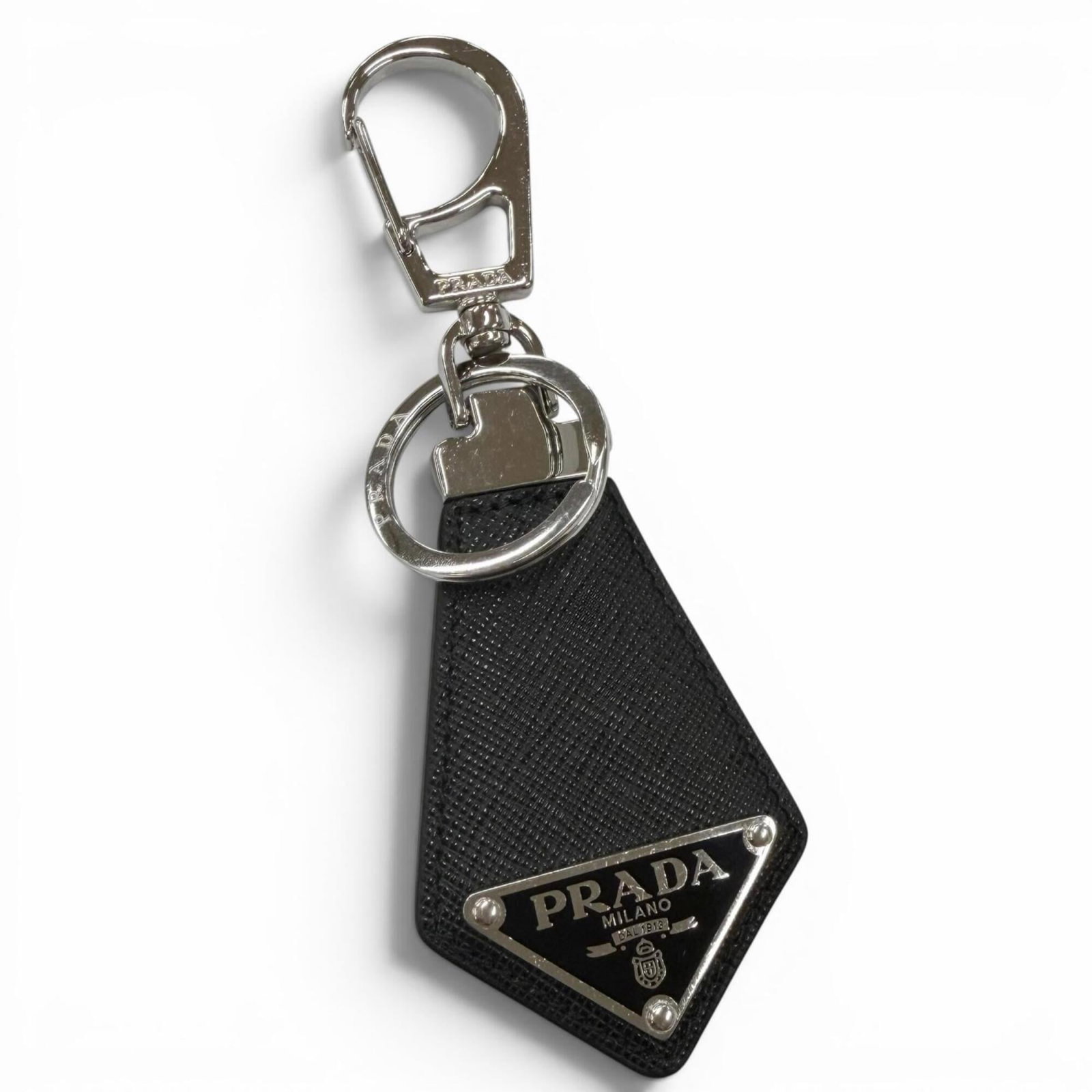 Keyring Leather By Prada: Keyring Leather By Prada Saffiano leather keyring from Prada, featuring a sleek black and silver design. With its durable construction and classic style, this keyring is a timeless accessory for