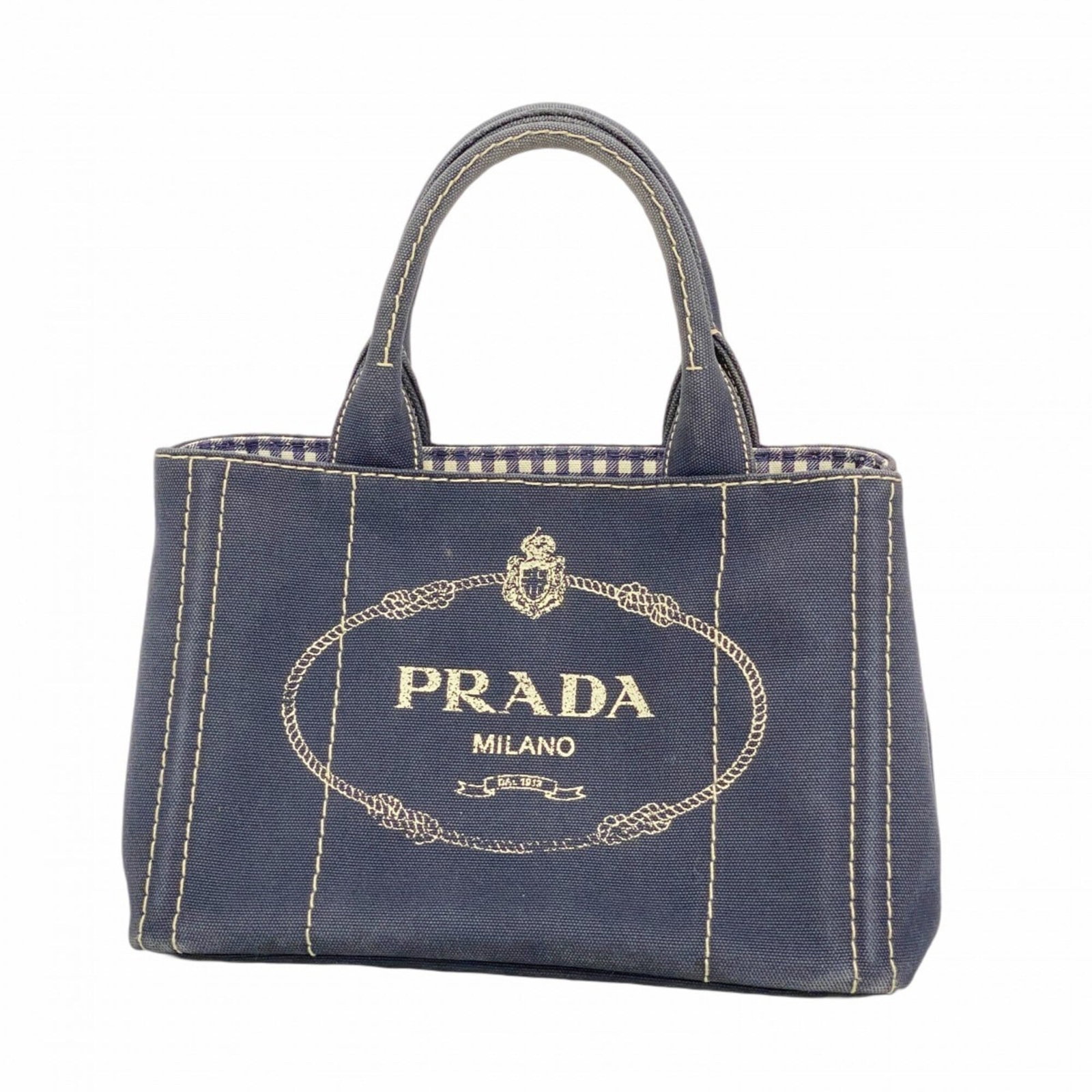 Canvas tote bag by Prada: Canvas tote bag by Prada Canvas tote bag by Prada, featuring navy canvas material and gold hardware. This used good condition bag has traces of usage with scratches and dirt visible, but remains in ov