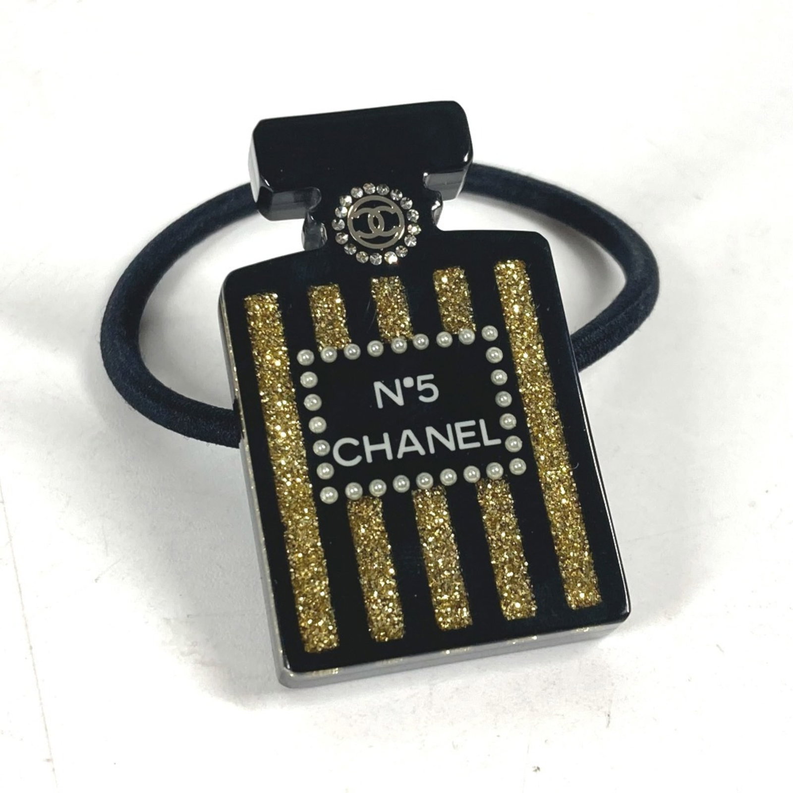 Hair tie by Chanel plastic: Hair tie by Chanel plastic Black and gold rhinestone charm hair tie by Chanel, made from durable plastic with a size of 2.8cm x 1.1''. This used item has hardly any traces of usage, presenting itself 