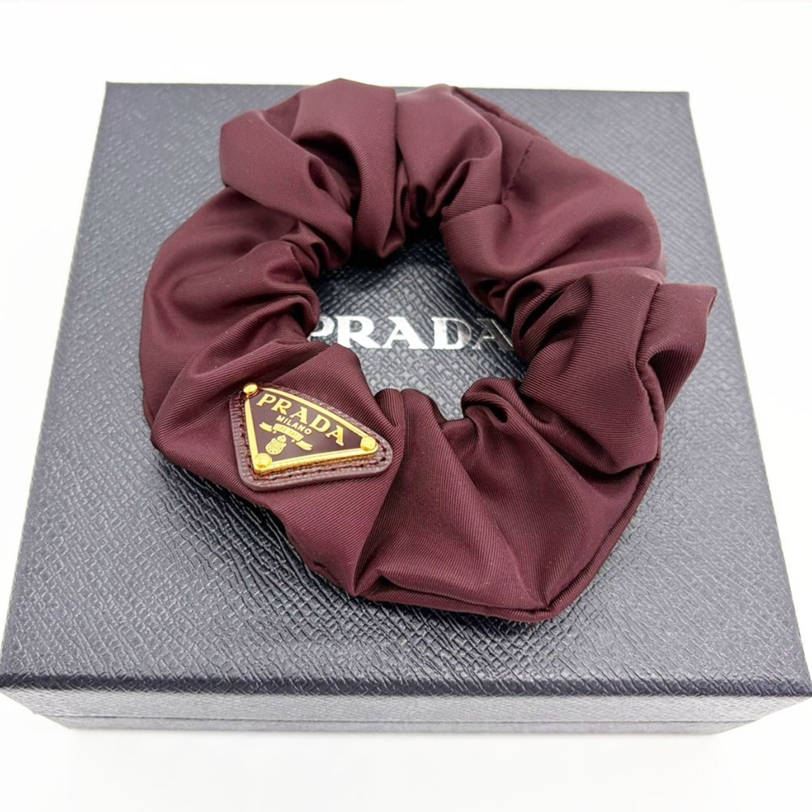 Nylon Scrunchie by Prada: Nylon Scrunchie by Prada Nylon Scrunchie by Prada features a Bordeaux color and measures 13cm x 5.11''. Made from nylon, this scrunchie boasts a sleek design that adds a touch of sophistication to