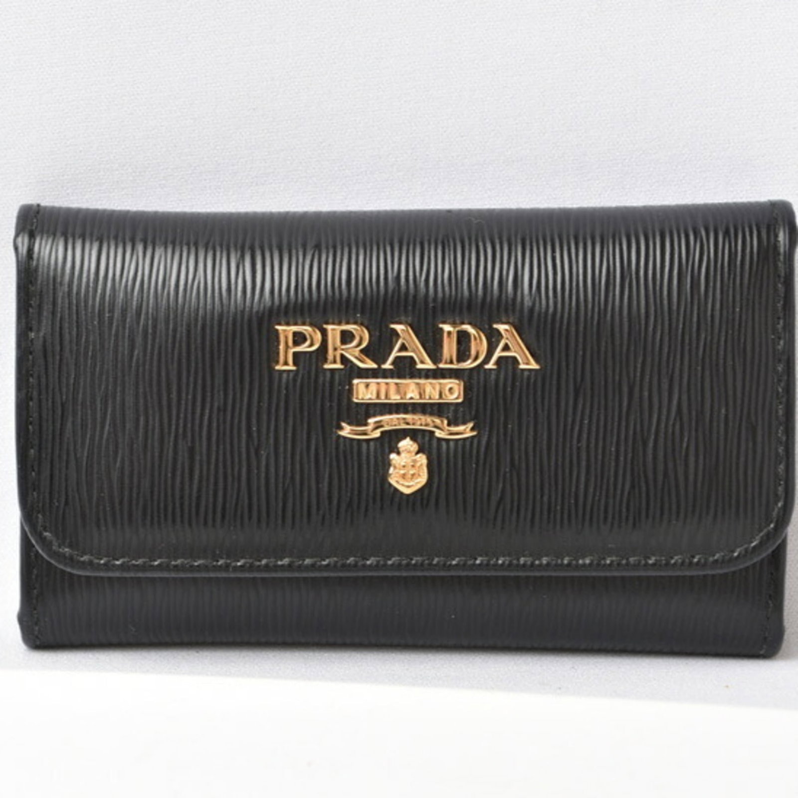 Prada leather keycase: Prada leather keycase Prada leather keycase with metal accents, featuring six key hooks and a compact design. The sleek, high-quality leather exterior provides a sophisticated touch to any purse or ba