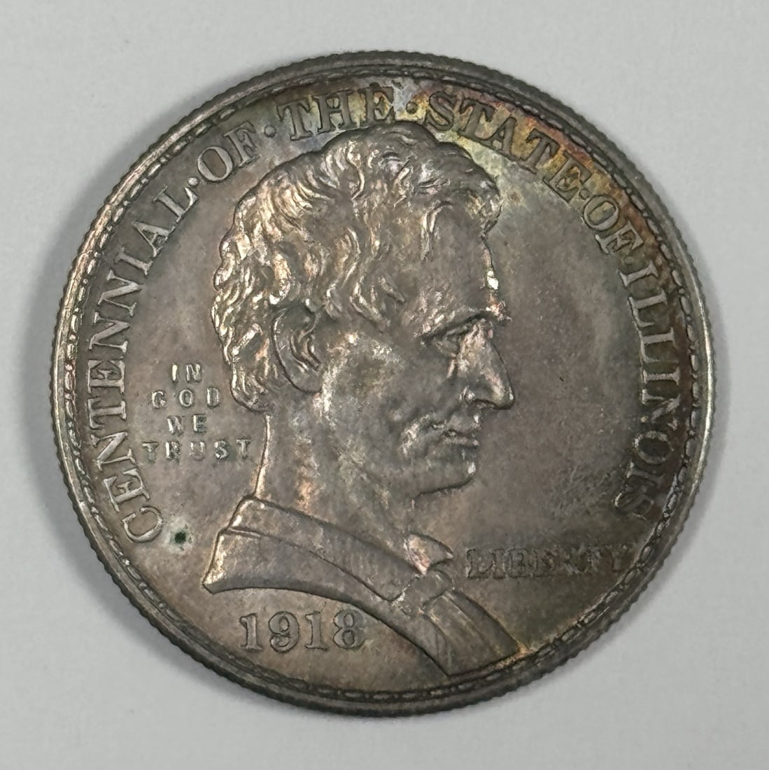 1918 LINCOLN COMMEORATIVE HALF DOLLAR AU/ BU PRETTY RAINBOW: 1918 LINCOLN COMMEORATIVE HALF DOLLAR AU/ BU PRETTY RAINBOW Circulated in 1918, this Lincoln Commemorative Half Dollar features a unique rainbow-colored patina, adding an eye-catching touch to its alr
