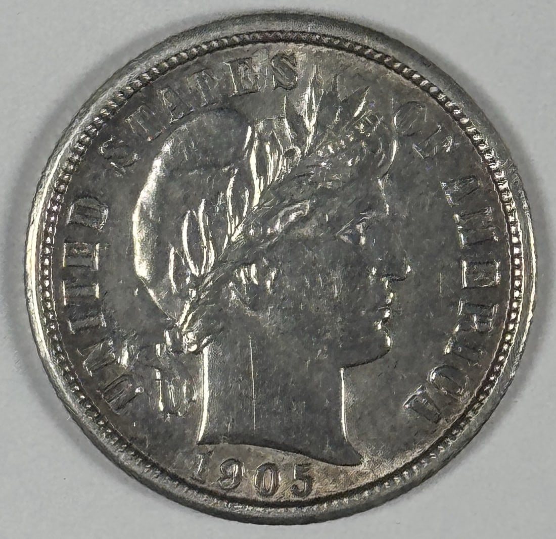 BARBER DIME AU 1905: BARBER DIME AU 1905 The 1905 Barber Dime features an iconic design with its classic portrait of Lady Liberty, surrounded by a wreath of oak leaves and laurel branches. This circulated coin is made of 