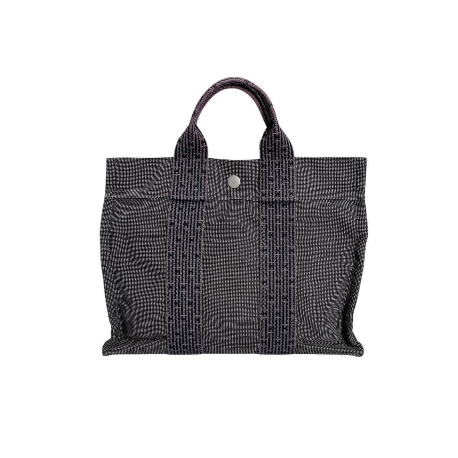 Canvas tote bag Hermes: Canvas tote bag Hermes Canvas tote bag from the iconic Hermes Line, crafted in high-quality canvas with a timeless gray hue. The bag features a sturdy zipper closure and a durable padlock for added