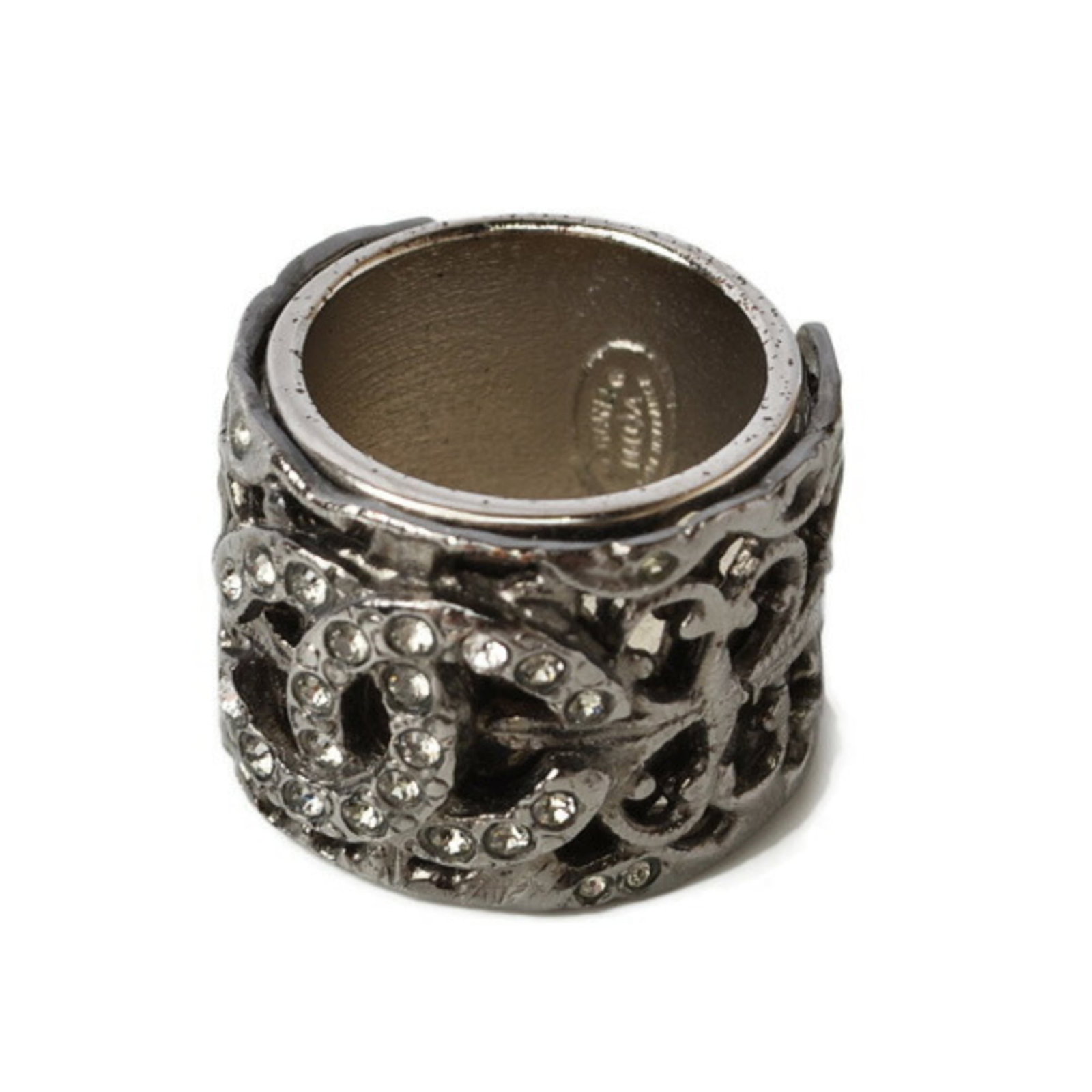 CHANEL Band Ring Metal Rhinestone: CHANEL Band Ring Metal Rhinestone Metal band ring from iconic French fashion brand CHANEL, adorned with a striking rhinestone design. This gently used piece features a gunmetal finish and showcases th