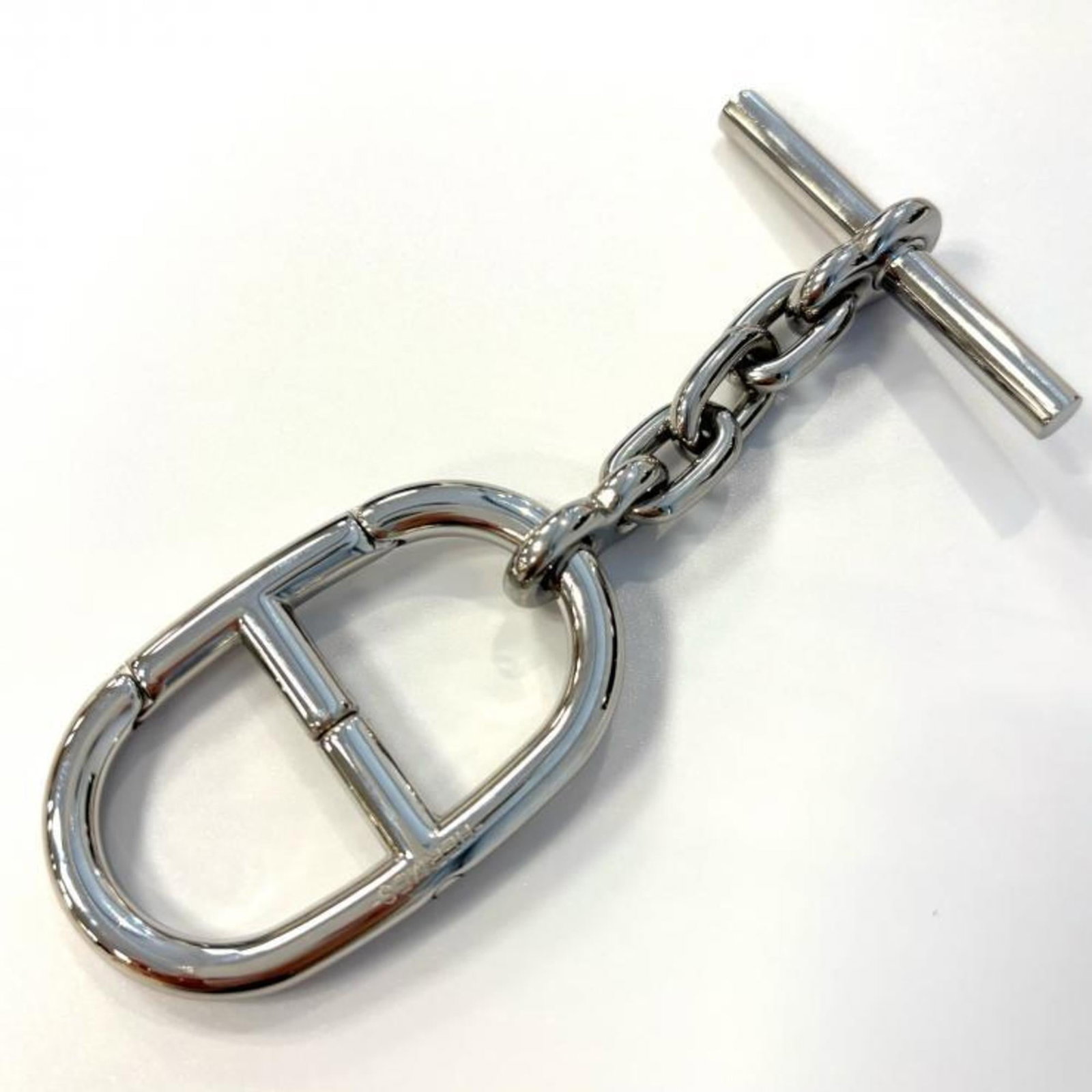 HERMES Handbag Charm Rhodium: HERMES Handbag Charm Rhodium Rhodium-plated charm from the iconic Hermes brand, featuring a sleek silver finish. This small charm measures 100mm x 30mm x 3.94'' x 1.18'' and bears visible signs of