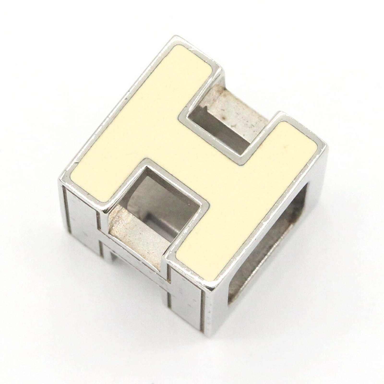 HERMES Enamel Metal: HERMES Enamel Metal Enamel metal pendant from the iconic Hermes brand, featuring a 12mm x 12mm cream-colored design. Gently used with minor signs of wear, this necklace pendant is in very good conditi