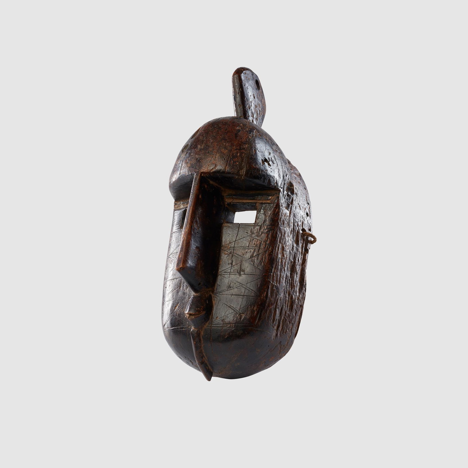 BAMANA MASK MALI: carved wood, the domed forehead with single crest above, the face deeply recessed with the square eyes parted by an angular ridged nose, pursed mouth and short beard, perforations to the sides for att