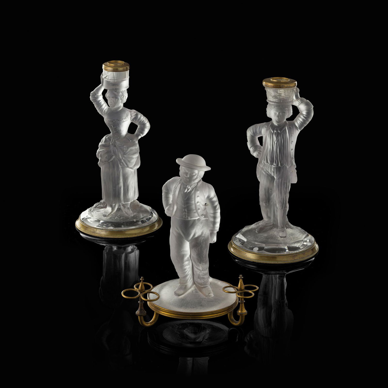 THREE MOULDED AND FROSTED GLASS FIGURES BY JOHN FORD,: THREE MOULDED AND FROSTED GLASS FIGURES BY JOHN FORD, HOLYROOD GLASS WORKS CIRCA 1870 comprising a PAIR OF CANDLESTICKS modelled as a male and a female each carrying a vessel upon their head and raise
