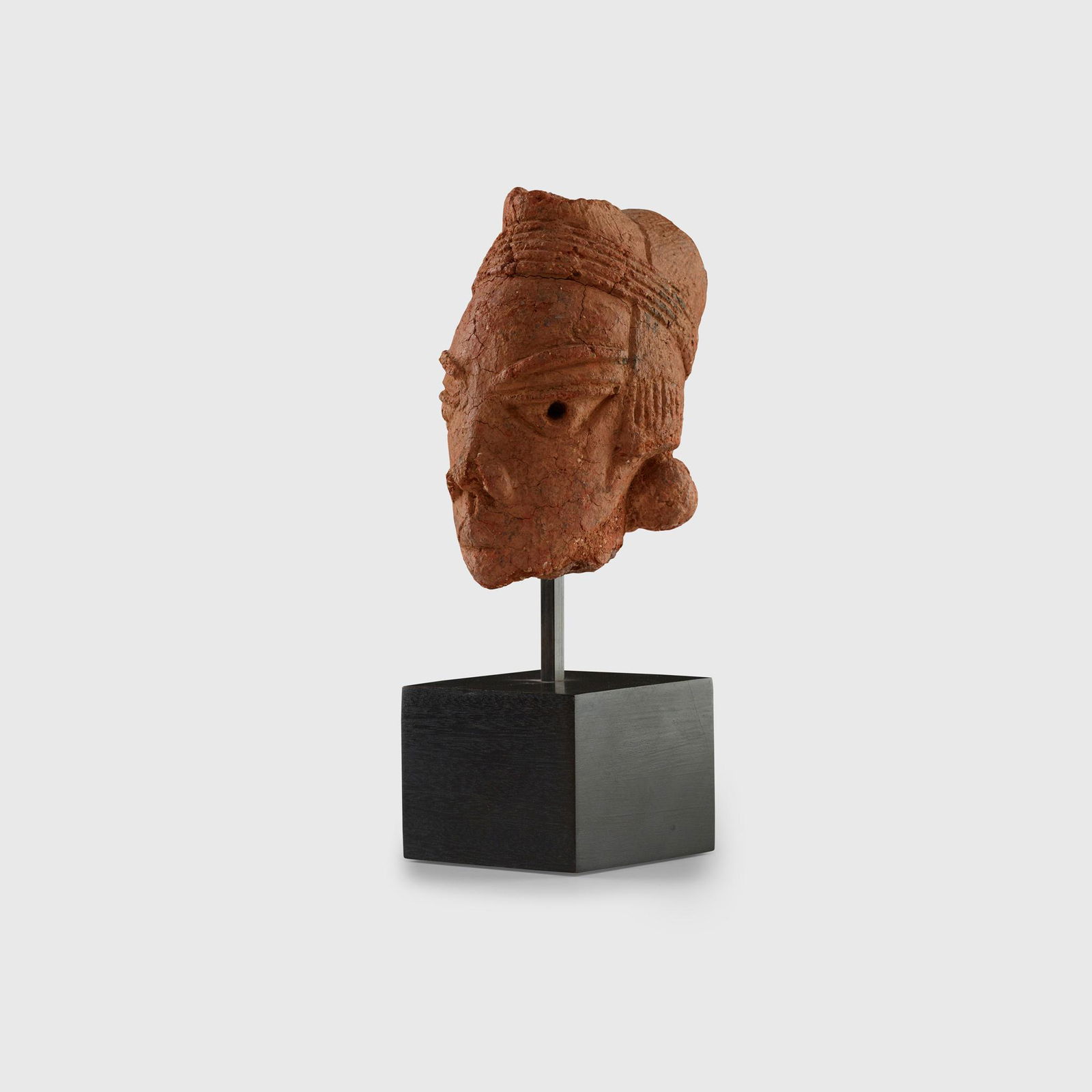 NOK HEAD NORTHERN NIGERIA, C. 500 B.C.: terracotta, the coiffure tied with a headband, broad eyes, flaring nostrils and pursed mouth, raised on a bespoke mount(11.5cm tall)Private collection, United Kingdom