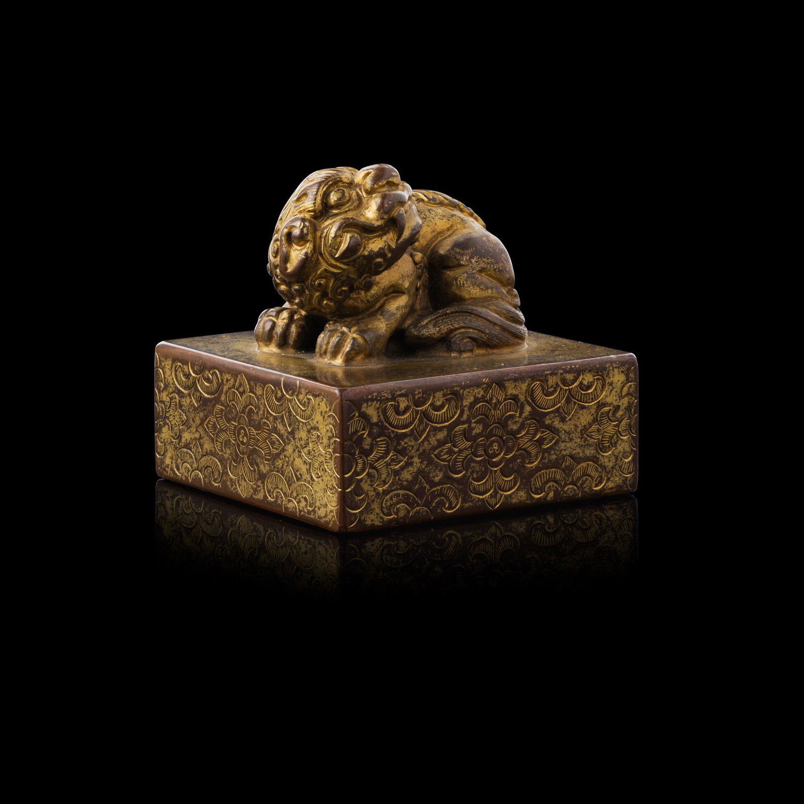 GILT-BRONZE SEAL: GILT-BRONZE SEAL 銅鎏金獅鈕方章 cast with a crouching lion looking back, mounted on a square plinth, sides of the plinth incised with repeated floral motif, t