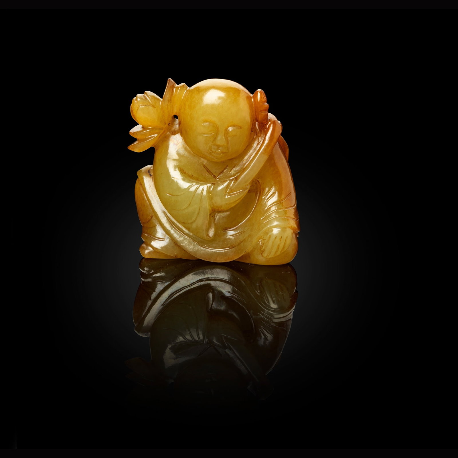 YELLOW JADE CARVING OF A BOY QING DYNASTY, 19TH CENTURY: YELLOW JADE CARVING OF A BOY QING DYNASTY, 19TH CENTURY 清 黃玉雕童子持蓮把件 carved in round with a seated boy carrying a large lotus and l