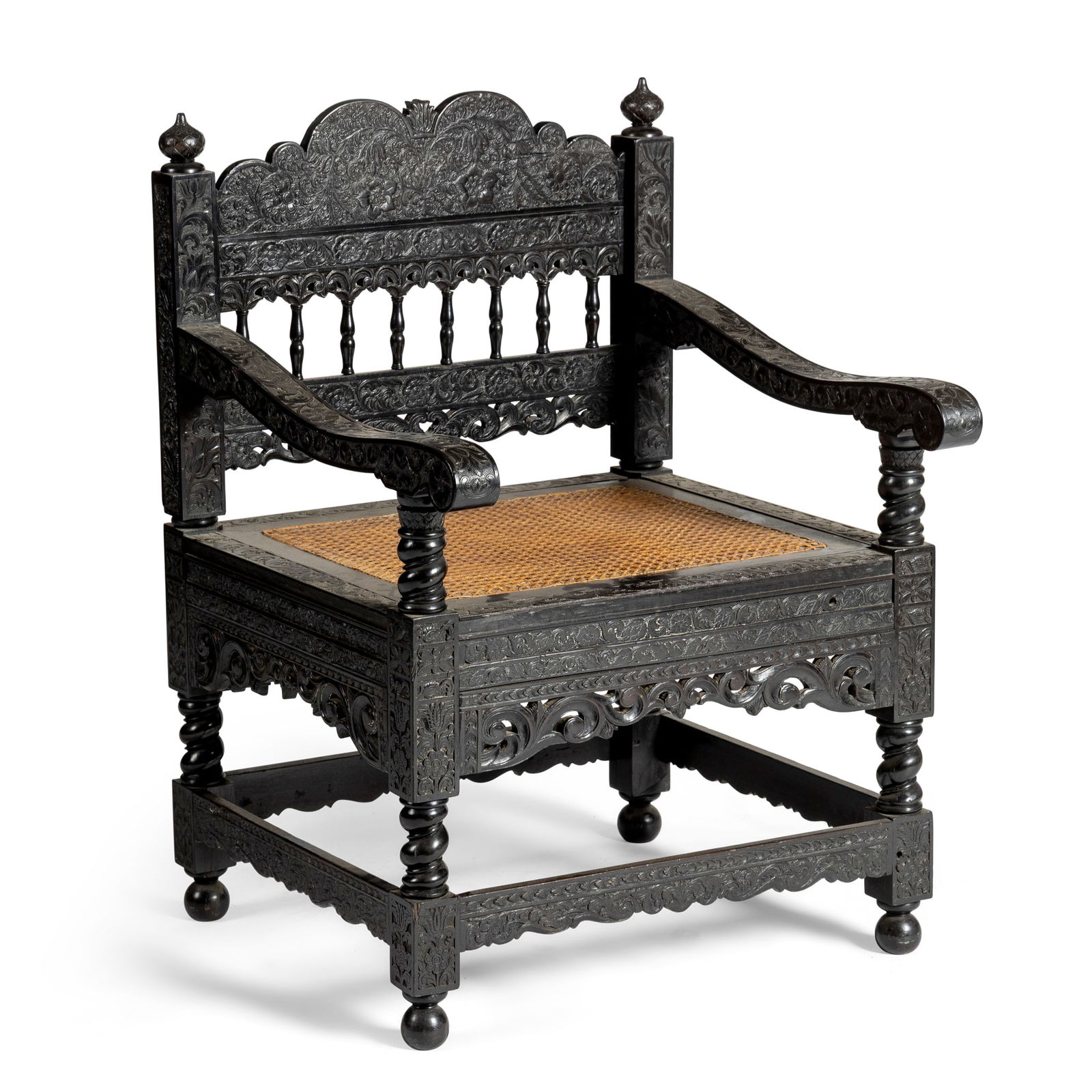 A DUTCH COLONIAL CEYLONESE ARMCHAIR: A DUTCH COLONIAL CEYLONESE ARMCHAIR 19TH CENTURY overall carved with foliate, floral and scrolling decoration, the arched back on spindle supports, down swept arms, drop-in caned seat on spiral-turned