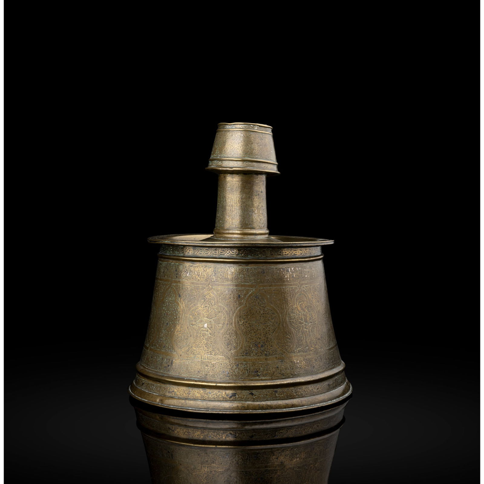 AN IMPORTANT MOSUL SILVER-INLAID BRASS CANDLESTICK: AN IMPORTANT MOSUL SILVER-INLAID BRASS CANDLESTICK MOSUL, FIRST HALF OF 13TH CENTURY the body of conical form with a cylindrical neck and socket of conical form, the drip-pan a later Ottoman replaceme