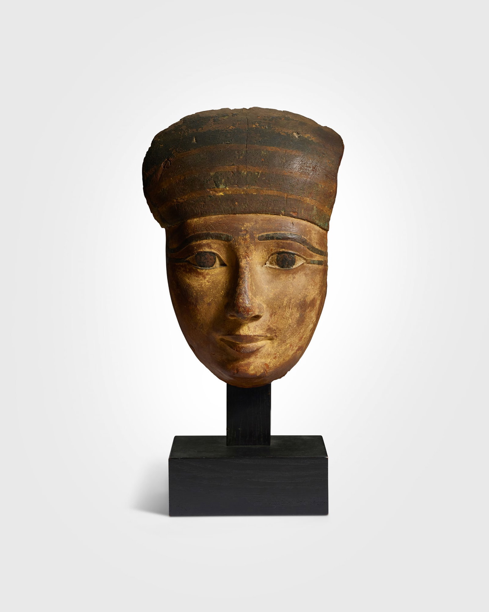 ANCIENT EGYPTIAN MUMMY MASK: ANCIENT EGYPTIAN MUMMY MASK EGYPT, THIRD INTERMEDIATE PERIOD, 22ND DYNASTY - 24TH DYNASTY, CIRCA 945 - 715 B.C. wood and pigment, the face painted in gold pigment and displaying softly rounded cheeks,