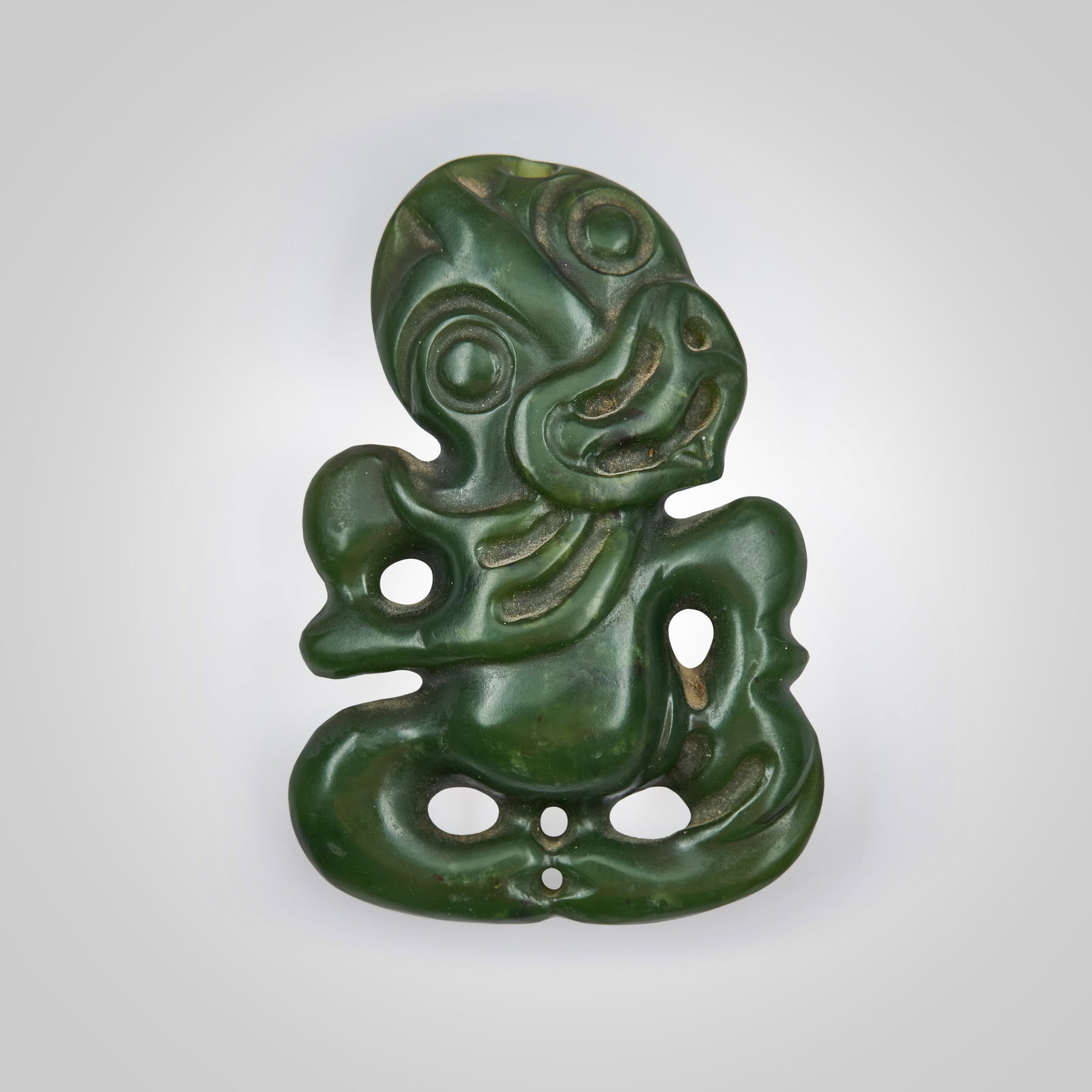 MAORI HEI-TIKI PENDANT: MAORI HEI-TIKI PENDANT NEW ZEALAND, 19TH CENTURY OR EARLIER carved pounamu, depicted with an open mouth displaying a forked tongue, the right hand resting on the chest and the left held to the thigh, 