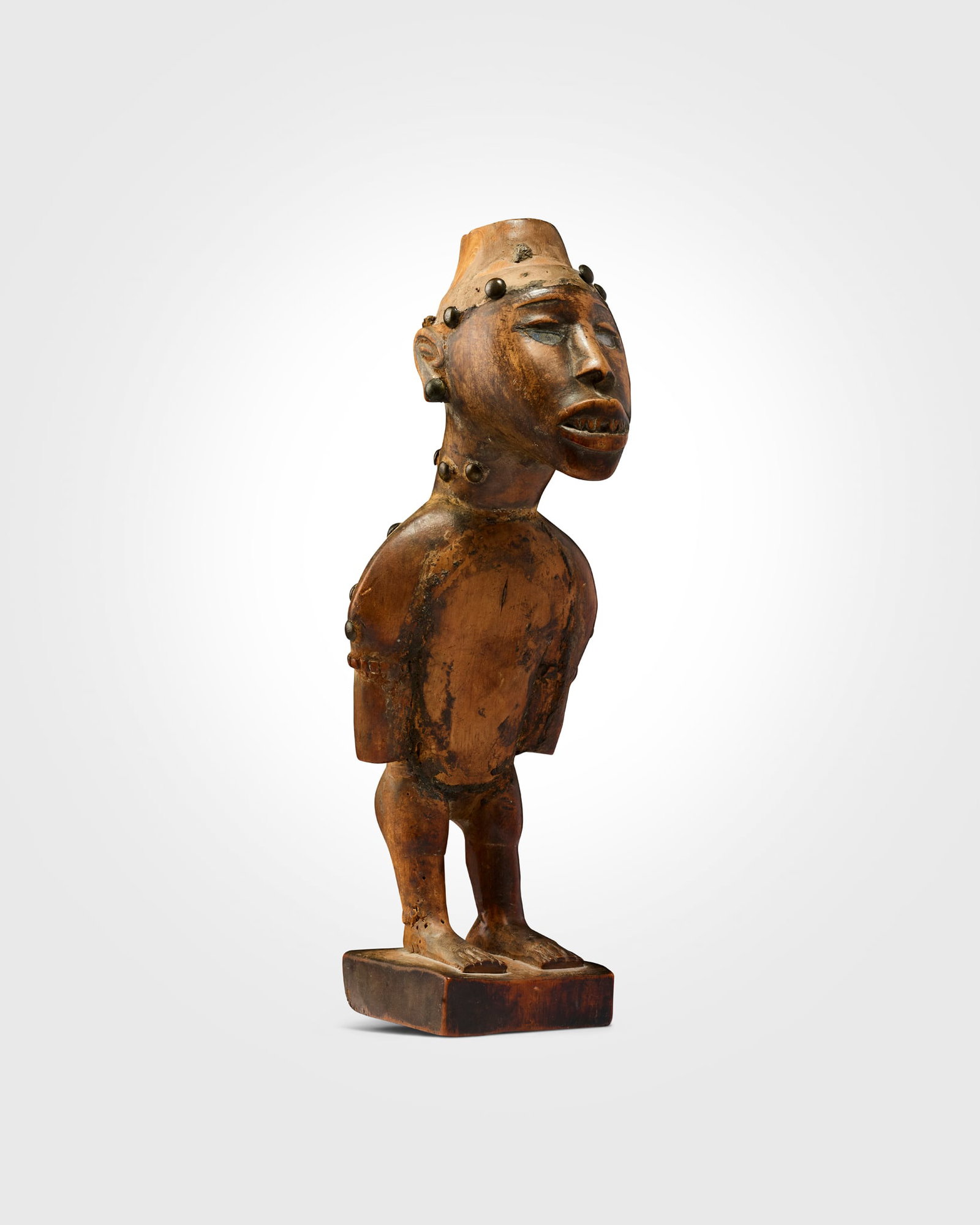 KONGO YOMBE NKISI FIGURE: KONGO YOMBE NKISI FIGURE DEMOCRATIC REPUBLIC OF CONGO carved wood and brass, shown standing, the torso angled forwards, the face expressive, with large open eyes inlaid with glass and emphasised by ar