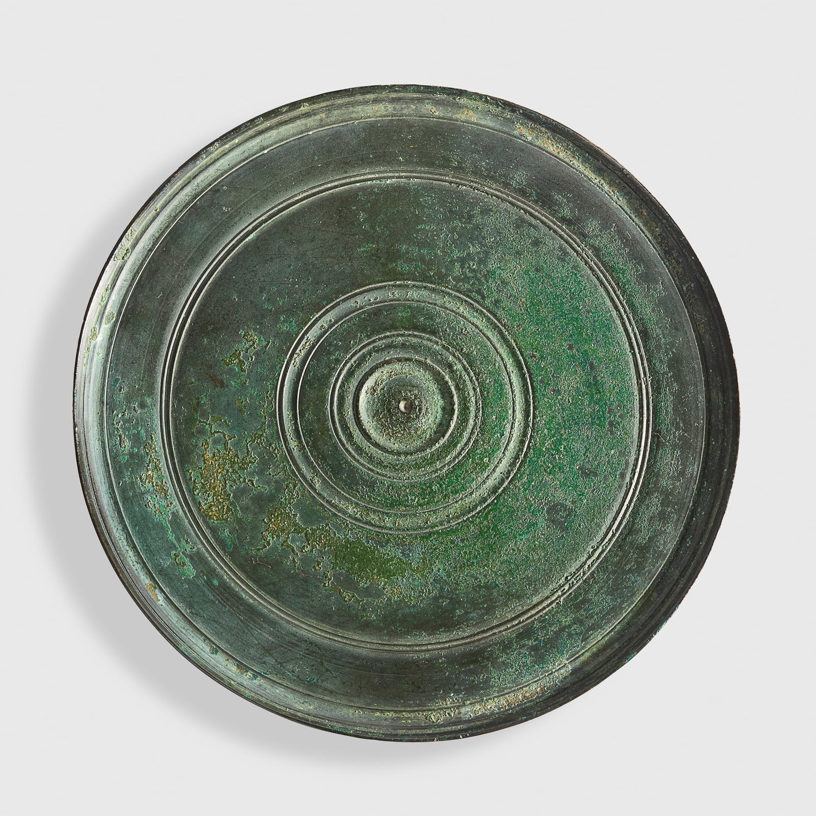 ROMAN BRONZE MIRROR: ROMAN BRONZE MIRROR EUROPE, C. 1ST - 2ND CENTURY A.D. bronze, a finely worked disc, with raised concentric bands along the border, deep green patination, raised on a bespoke mount 16cm diameter Privat