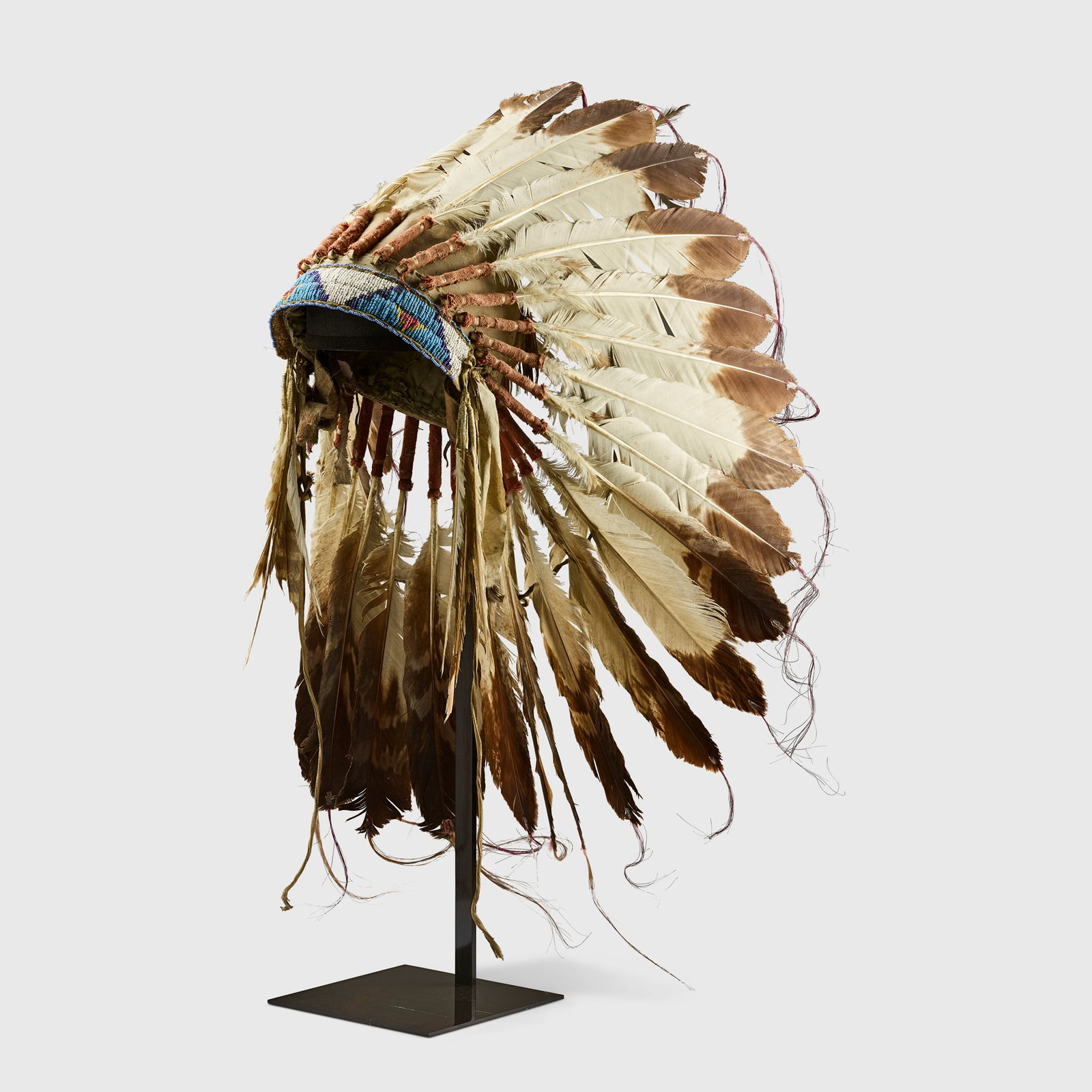LAKOTA SIOUX HEADDRESS: LAKOTA SIOUX HEADDRESS GREAT PLAINS, UNITED STATES OF AMERICA, C. 19TH CENTURY felt, cotton, red fabric, seed beads of various hues, feathers, bison hide, leather, horsehair, satin ribbon 43.4cm tall 