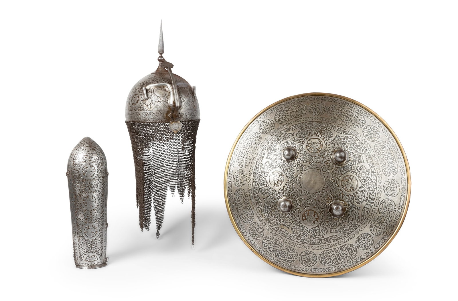 A QAJAR SET OF STEEL ARMOUR: A QAJAR SET OF STEEL ARMOUR PERSIA, 19TH CENTURY comprising a shield, helmet and armband, each profusely engraved and decorated with figural and animal medallions on a reserve of floral and leafy tend