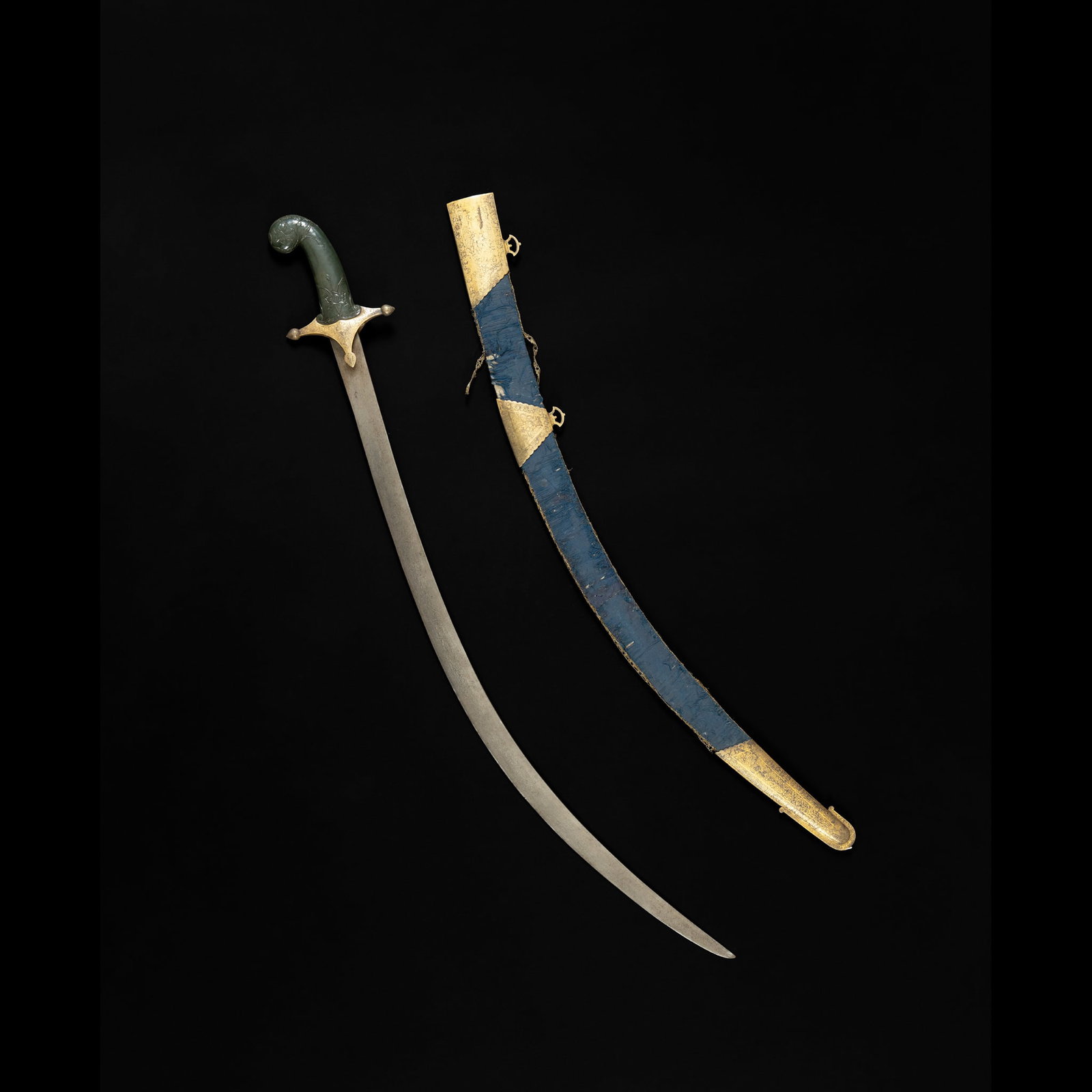 A MUGHAL JADE-HILTED STEEL SWORD (TALWAR): A MUGHAL JADE-HILTED STEEL SWORD (TALWAR) INDIA, 17TH CENTURY AND LATER the single-edged slender watered steel blade and gilt-copper cross-guard set with a spinach coloured jade hilt carved with 