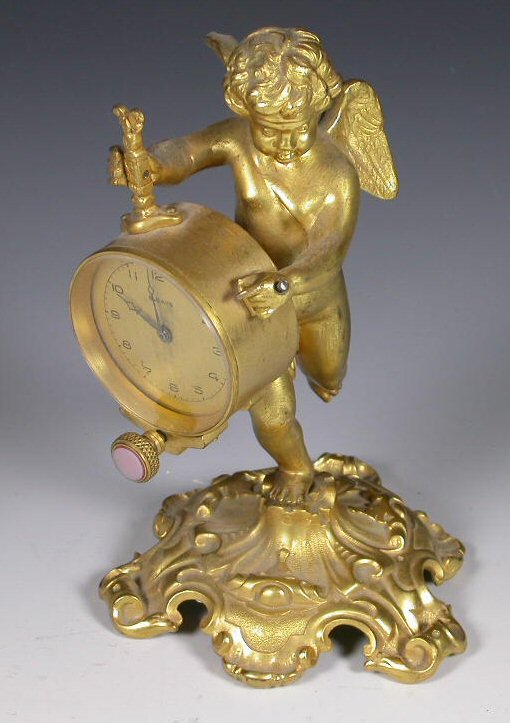 A gilt brass mantel clock, modelled as a winged p: A gilt brass mantel clock, modelled as a winged putto holding the circular dial, on scrolled base 17.5cm high 282 A green painted and gilt wooden clock case, with associated movement, 17cm high; and a