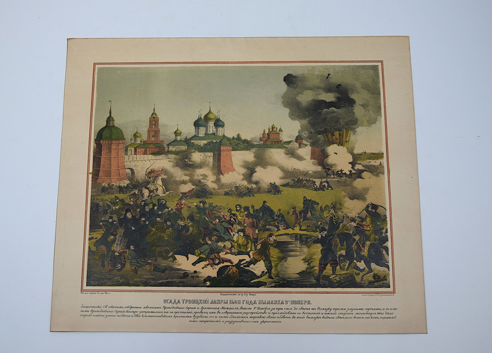 1865 RUSSIAN HISTORICAL LITHOGRAPH – SIEGE OF TROITSKAYA LAVRA: A COLOR LITHOGRAPHIC PRINT DEPICTING A DRAMATIC SCENE FROM THE SIEGE OF THE TROITSKAYA (TRINITY) LAVRA, SHOWING FIGURES IN COMBAT BEFORE MONASTERY WALLS WITH EXPLOSIONS AND SMOKE; WITH CYRILLIC TEXT B