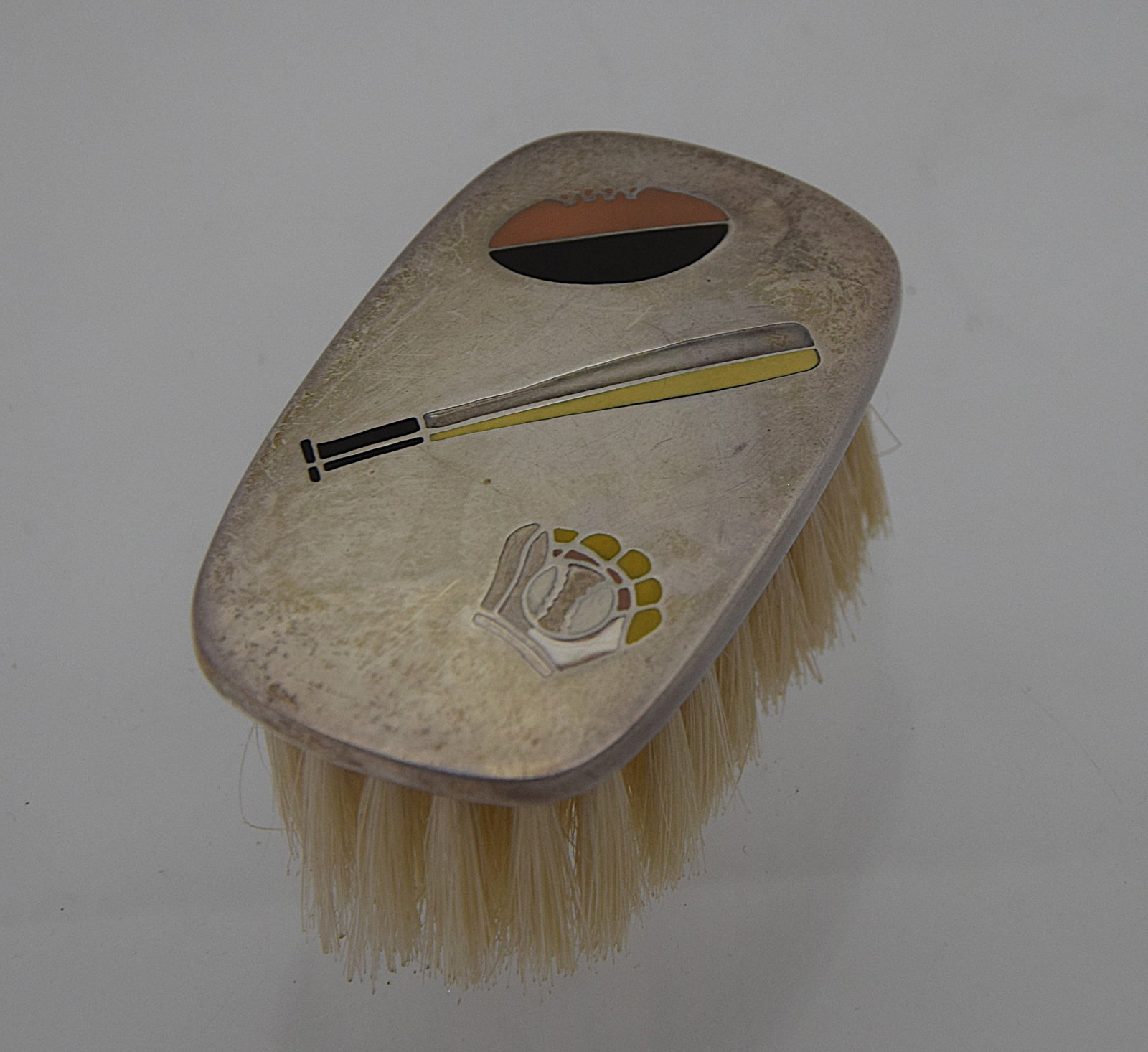 STERLING SILVER AND ENAMEL HAIR BRUSH: DECORATIVE HAND BRUSH WITH STERLING SILVER BACK, THE SURFACE INLAID WITH STYLIZED DESIGN ELEMENTS INCLUDING A BASEBALL, BAT, AND GLOVE IN COLORED ENAMEL, THE REVERSE FITTED WITH LIGHT-COLORED BRISTLES