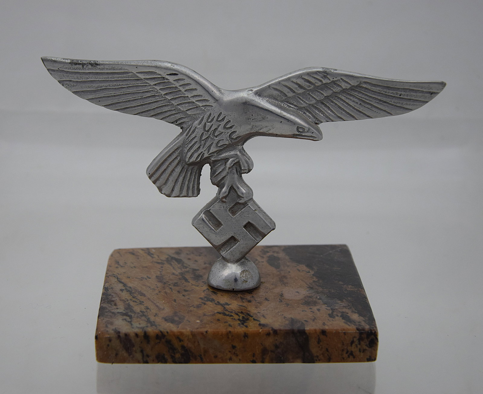 WWII LUFTWAFFE (AIR FORCE) GERMAN EAGLE WITH SWASTIKA DESK ORNAMENT ON STONE BASE: ORIGINAL THIRD REICH PERIOD LUFTWAFFE (AIR FORCE) METAL DESK ORNAMENT FEATURING A SPREAD-WING EAGLE CLUTCHING A SWASTIKA, MOUNTED ON A POLISHED STONE OR MARBLE BASE; CAST METAL CONSTRUCTION WITH SILVE