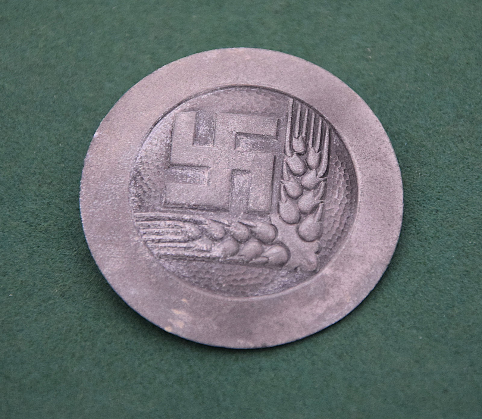 WWII GERMAN THIRD REICH TINNIES / BADGE: ORIGINAL PERIOD GERMAN TINNIE-STYLE BADGE FEATURING A CENTRAL DEVICE WITH SWASTIKA AND AGRICULTURAL MOTIFS (SHEAF OF WHEAT), SET WITHIN A RAISED CIRCULAR BORDER; PRESSED METAL CONSTRUCTION WITH A MATT
