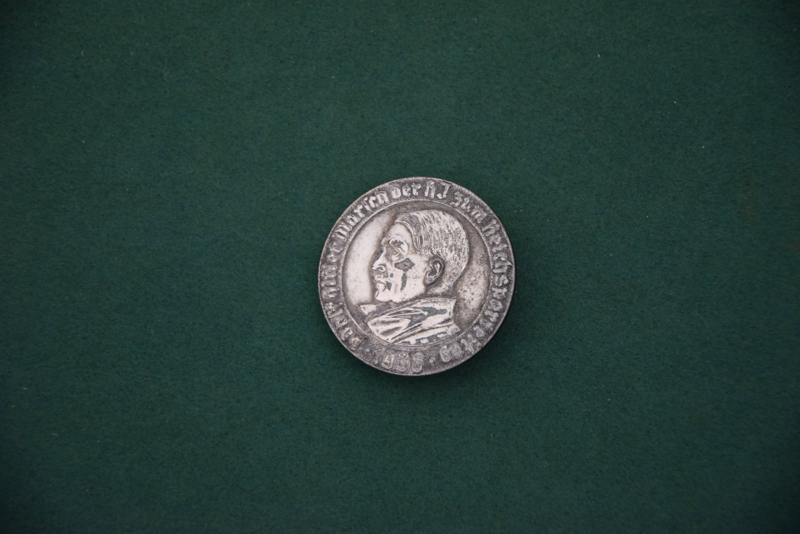 THIRD REICH ADOLF HITLER COMMEMORATIVE PIN: ORIGINAL CIRCULAR METAL LAPEL BADGE FEATURING PROFILE PORTRAIT OF ADOLF HITLER WITH SURROUNDING INSCRIPTION; REVERSE MARKED “PAULMANN & CRONE, LÜDENSCHEID” AND “GES. GESCH.” WITH HORI
