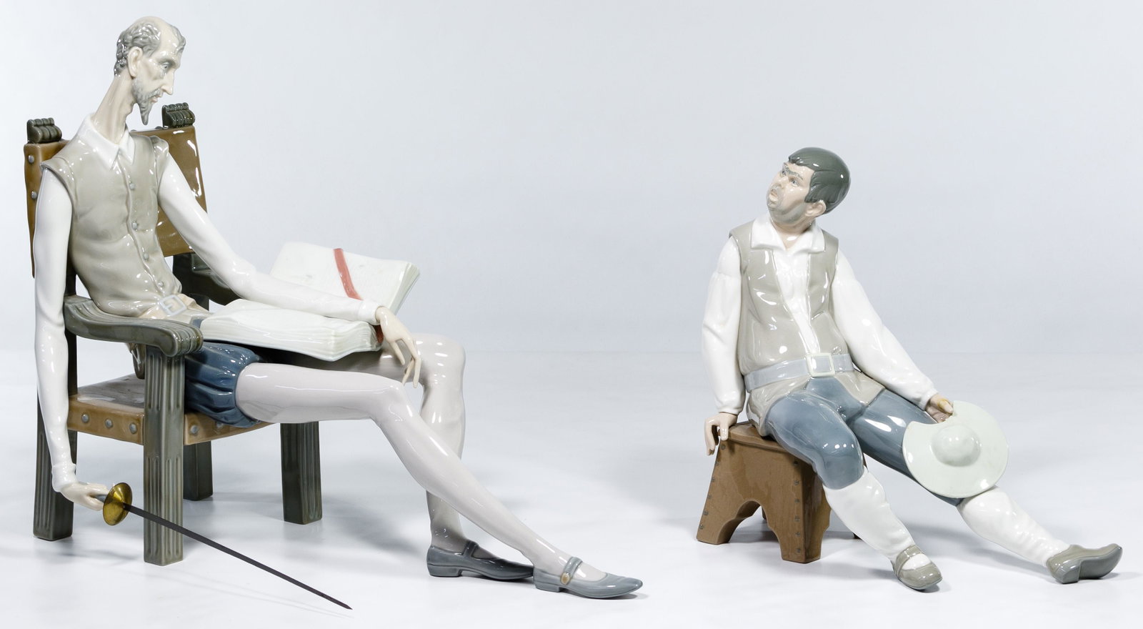 Lladro #1030 'Don Quixote' and #1031 'Sancho Panza': Lladro #1030 'Don Quixote' and #1031 'Sancho Panza' Figurines Two retired items, Don Quixote sitting in chair with book and sword and Sancho Panza sitting on bench holding his hat; marked Lladro Diasa