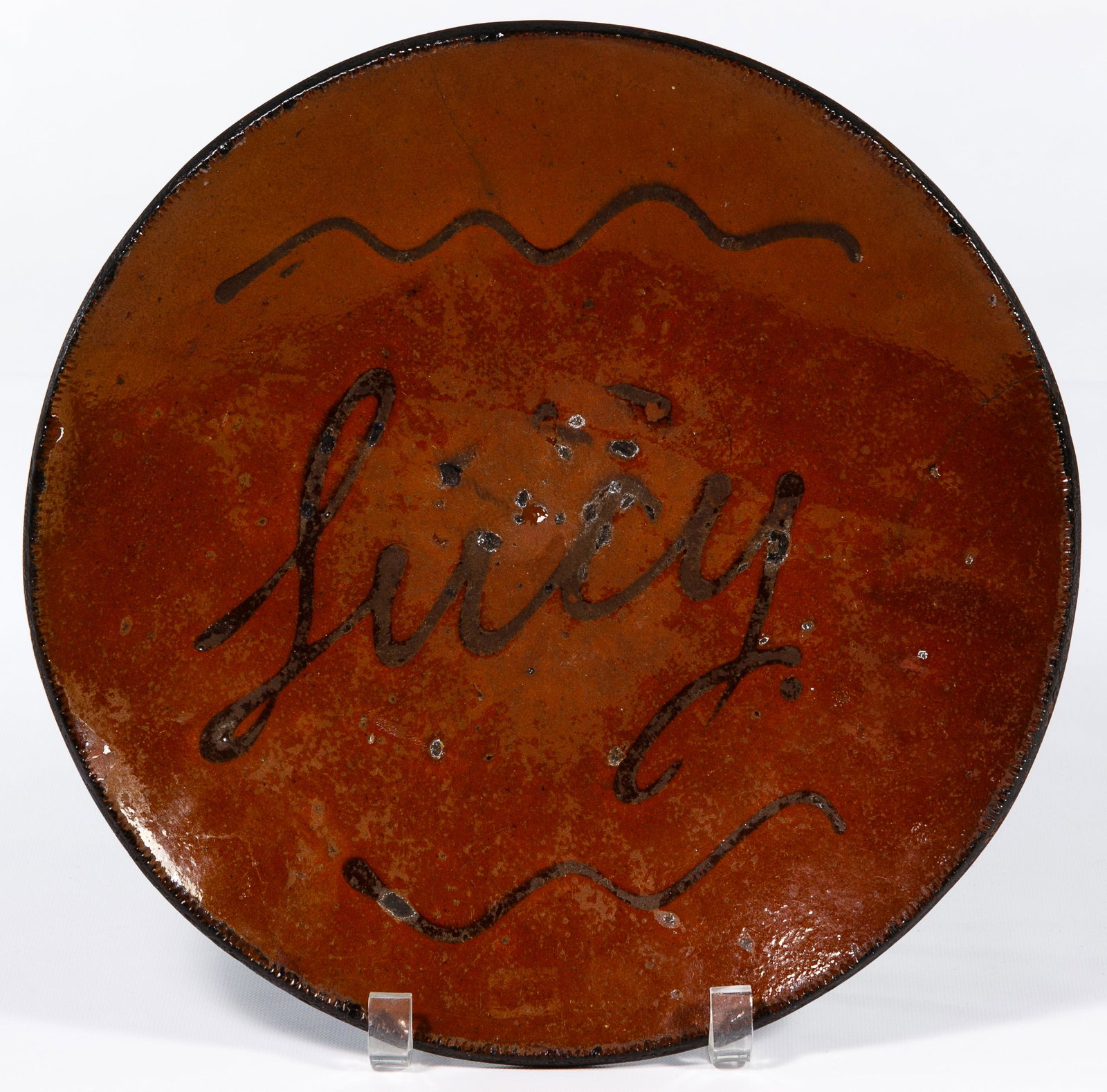 Pennsylvania Redware Slip Charger: Pennsylvania Redware Slip Charger 19th Century, having slip decoration and the name 'Lucy'; silver letter and numbers on the back Condition: Good, color loss throughout; small chips along edges; two c