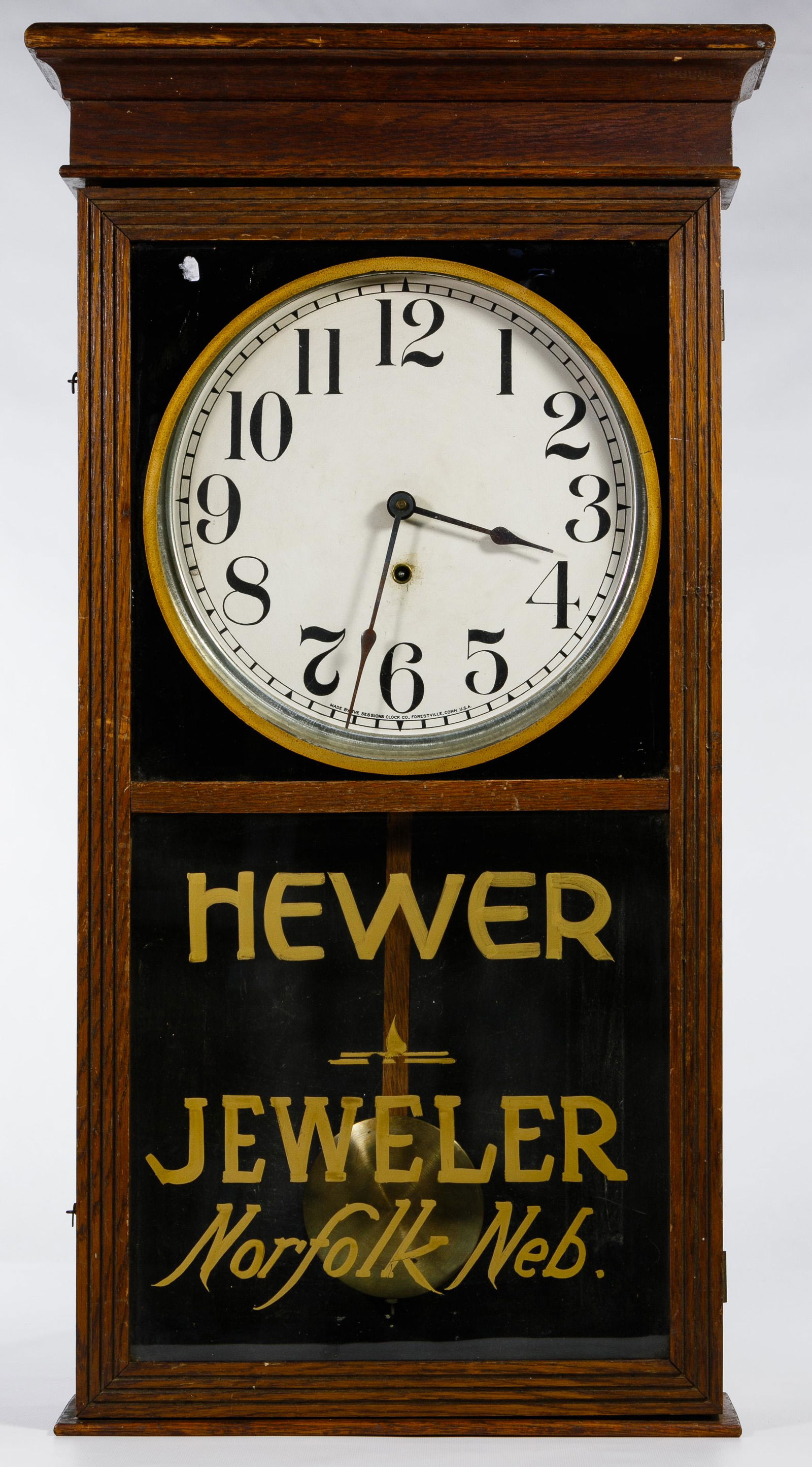 Sessions Advertising Regulator Wall Clock: Sessions Advertising Regulator Wall Clock Sessions Clock Co. Regulator #2 having an oak case and a reverse painted glass reading 'Hewer Jeweler Norfolk, Neb.', an eight day movement and a twelve inch