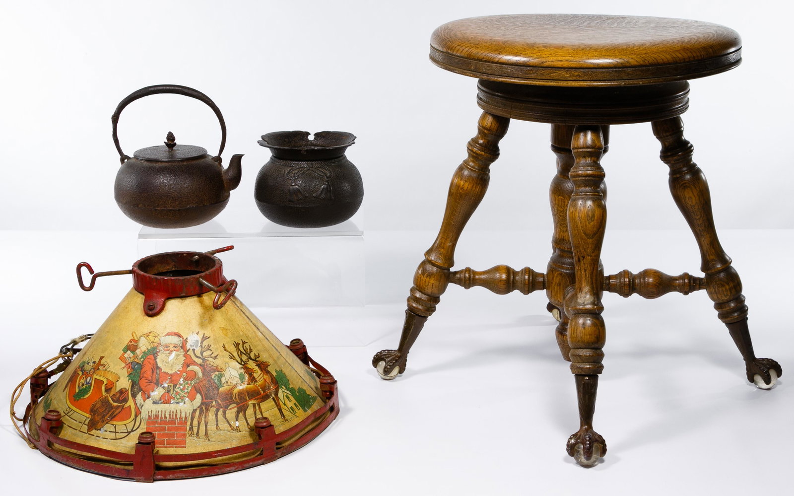 Piano Stool, Christmas Tree Stand and Cast Iron Pot: Piano Stool, Christmas Tree Stand and Cast Iron Pot Assortment Wood piano stool having ball and claw feet of metal and glass; a metal, painted Christmas tree stand depicting Santa in sleigh with reind