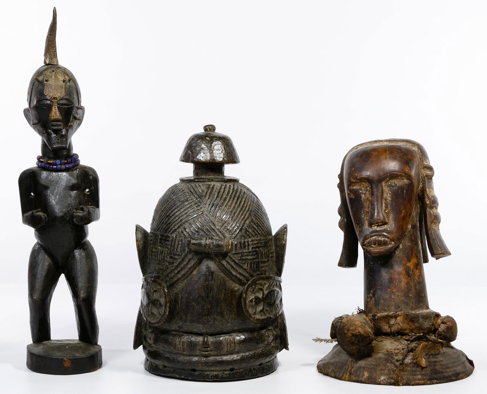African Wood Carving Assortment: African Wood Carving Assortment Including a Fang reliquary head mounted on a basket and having attached feathers and fetish bundles; a Songye Nkisi horn fetish figure having metal face attachments and