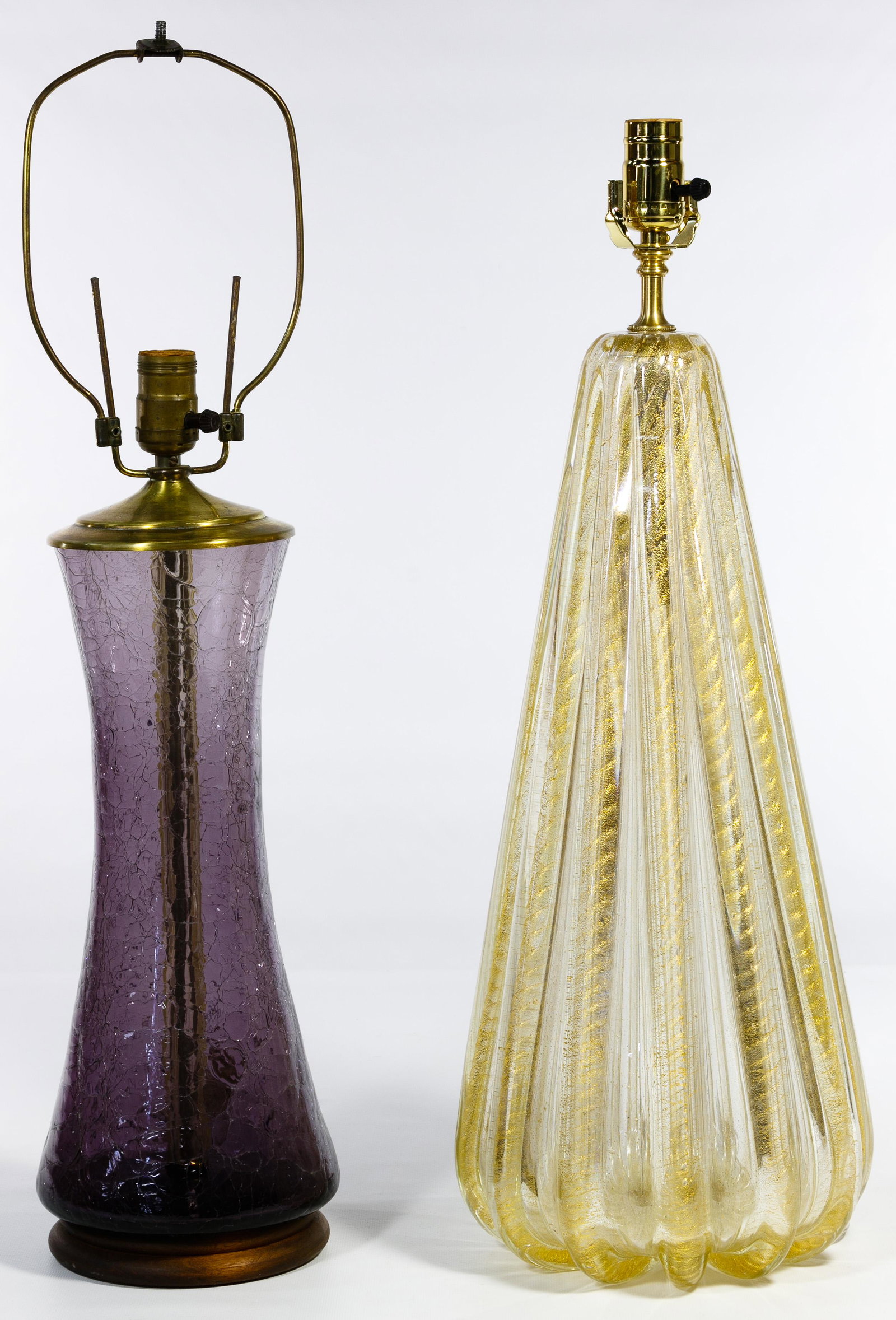 Blenko and Murano Style Glass Lamps: Blenko and Murano Style Glass Lamps Two lamps including a Blenko style purple crackle glass having a wood base with brass top, glass finial and hardware; and a Murano style having clear glass with met
