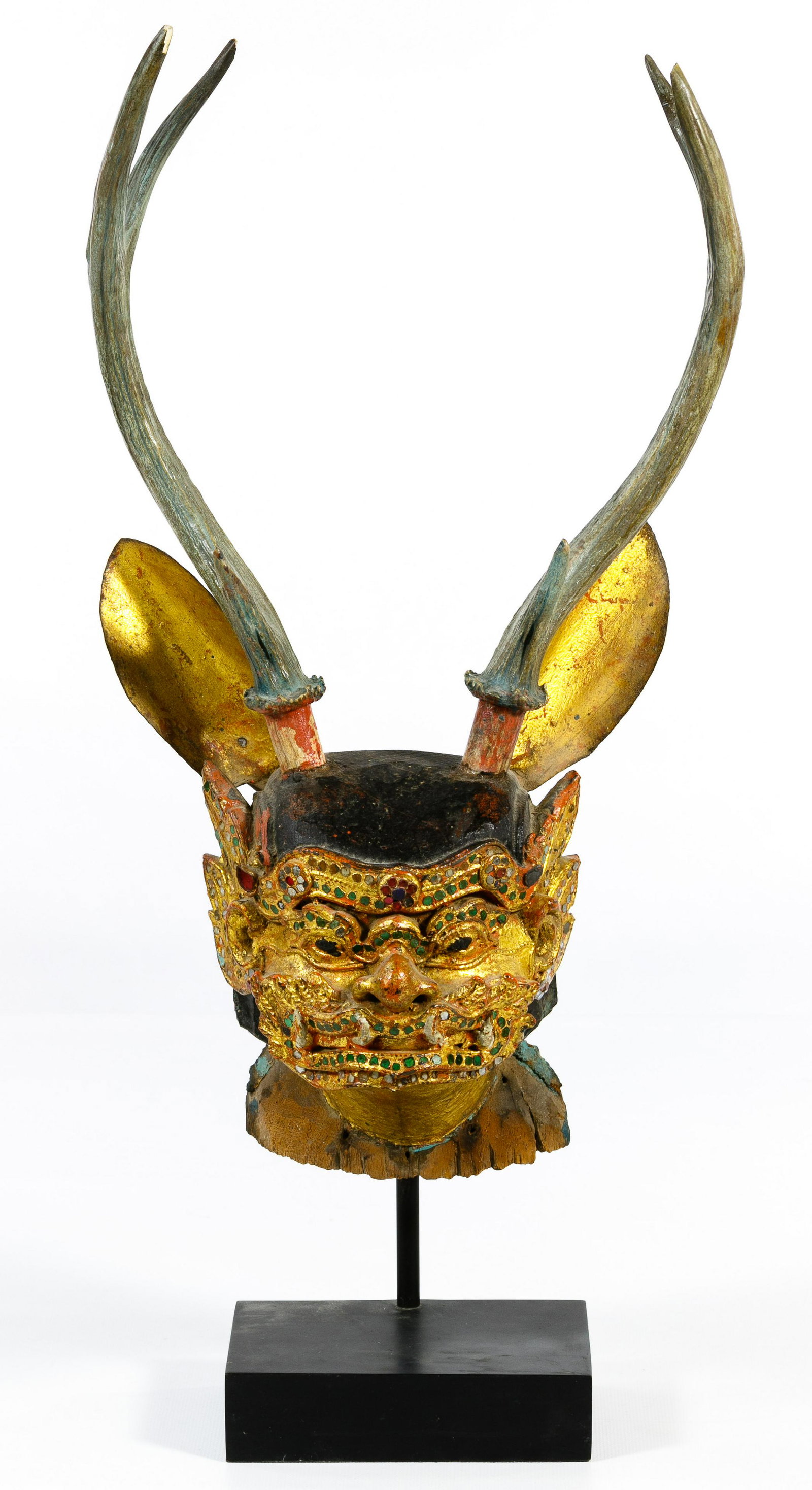 Burmese Mandalay Period Carved Wood Puppet Head: Burmese Mandalay Period Carved Wood Puppet Head Depicting the head of a stag having metal ears, gold, red, black and blue paint and decorated with multi-colored bits of glass; mounted on a black stand