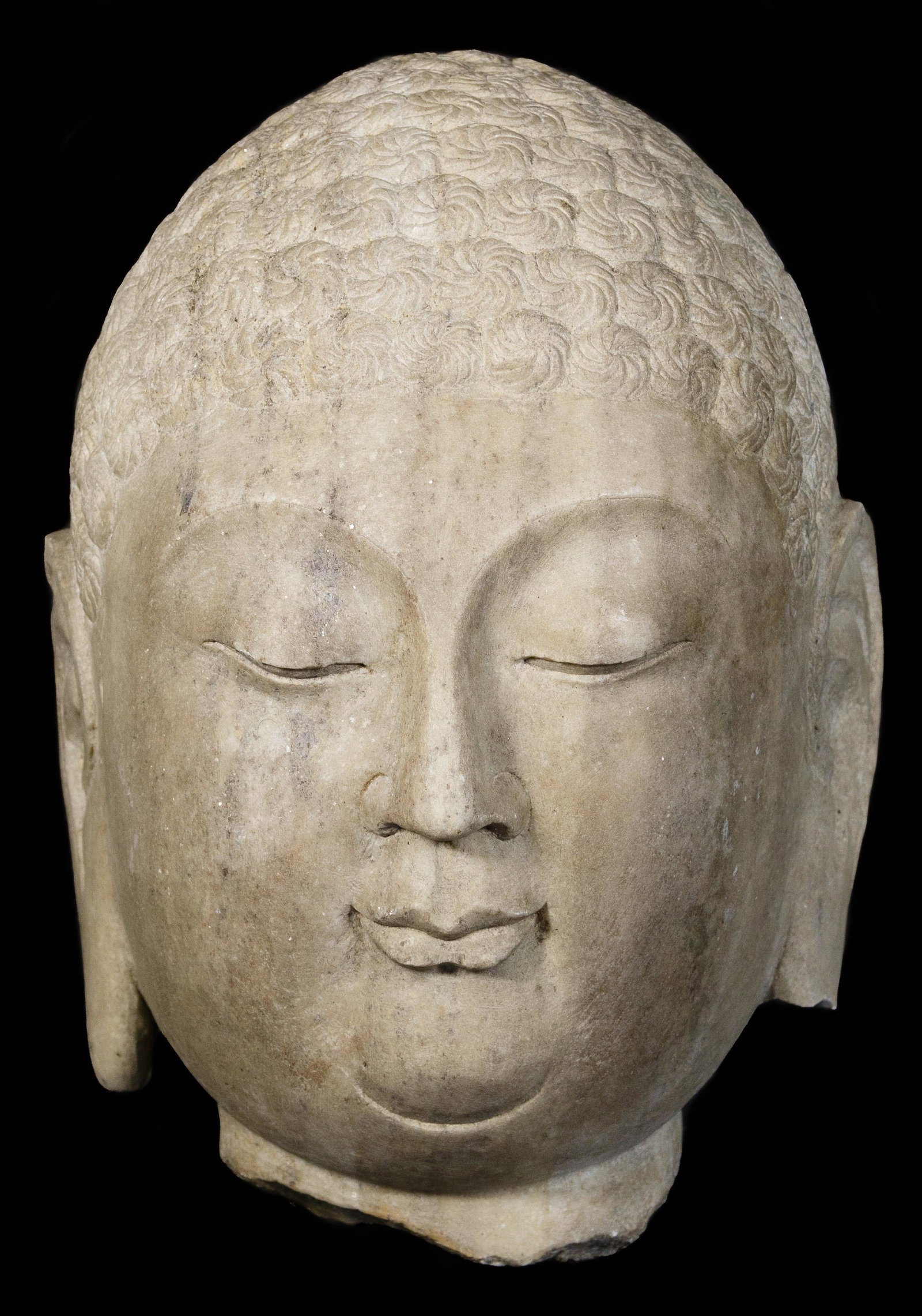 Chinese Carved Limestone Head of Buddha: Chinese Carved Limestone Head of Buddha Having dark grey veining in the stone and an uncarved back side; labeled 'Made in China' Condition: Good, chipping on edges of both ears; right ear missing lobe