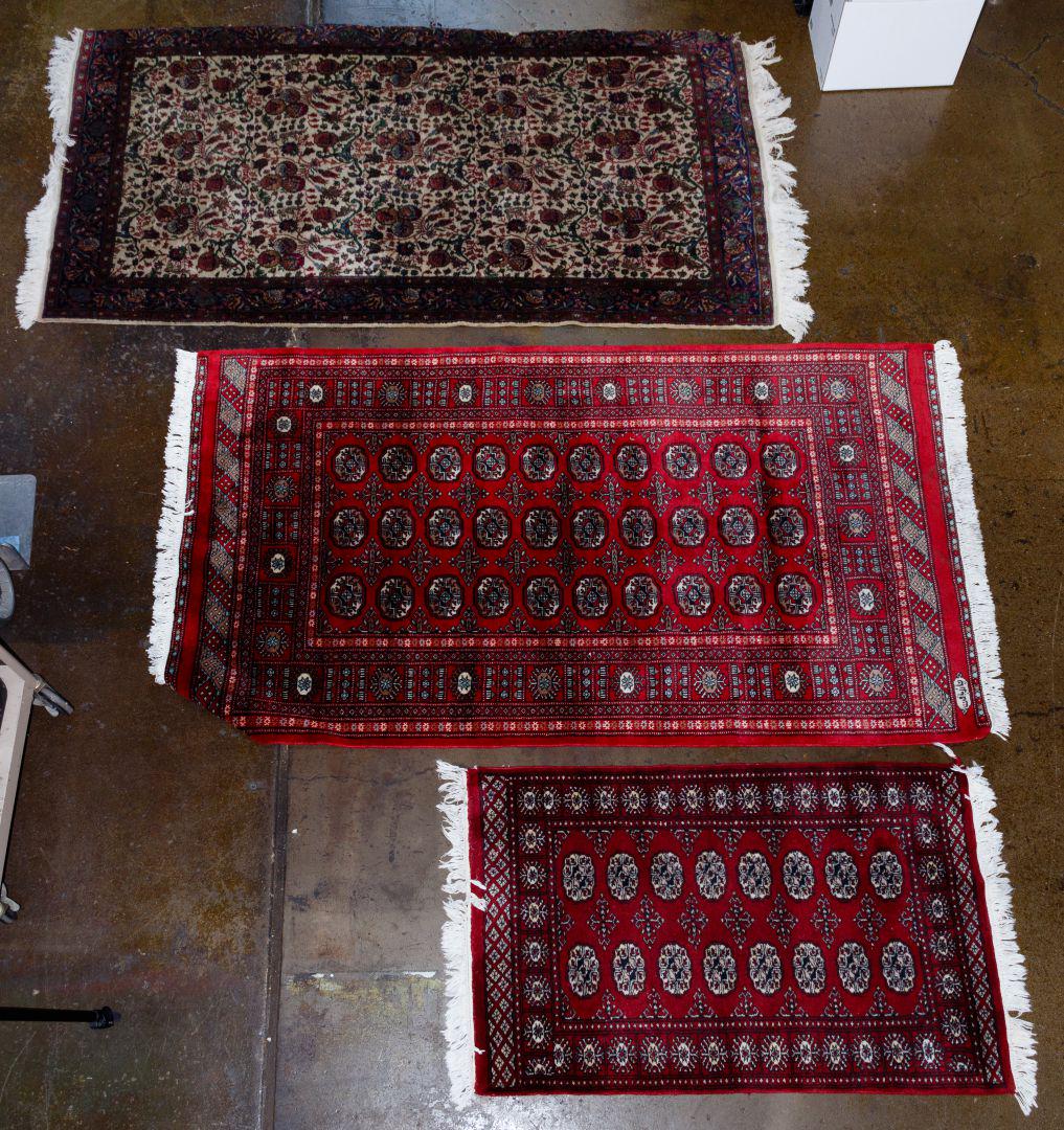 Rug Assortment: Rug Assortment Three items including a red and black wool rug made in Pakistan with fringe, a red and black woolen prayer rug with fringe, a woolen navy blue border with cream and various shades of cr